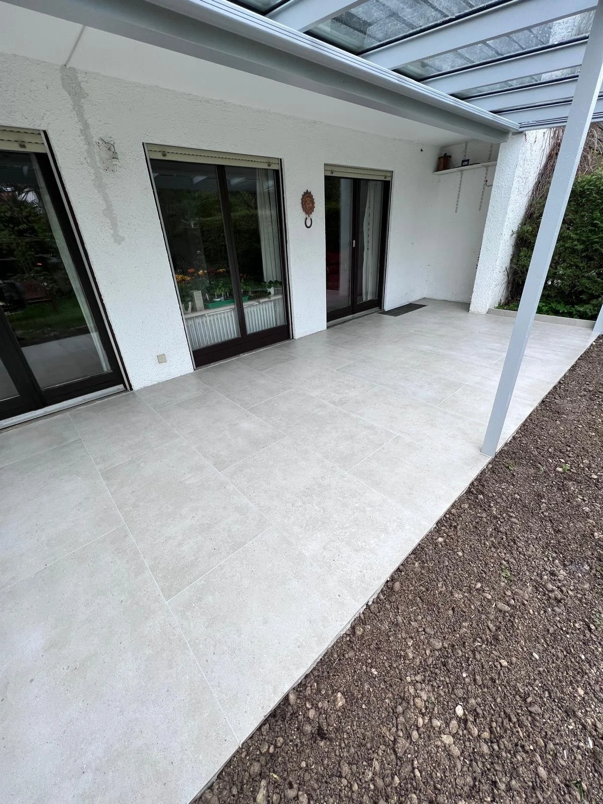 Blick auf eine verglaste Terrasse vor einem weißen Haus mit großen Doppelfenstern und einer Schiebetür.