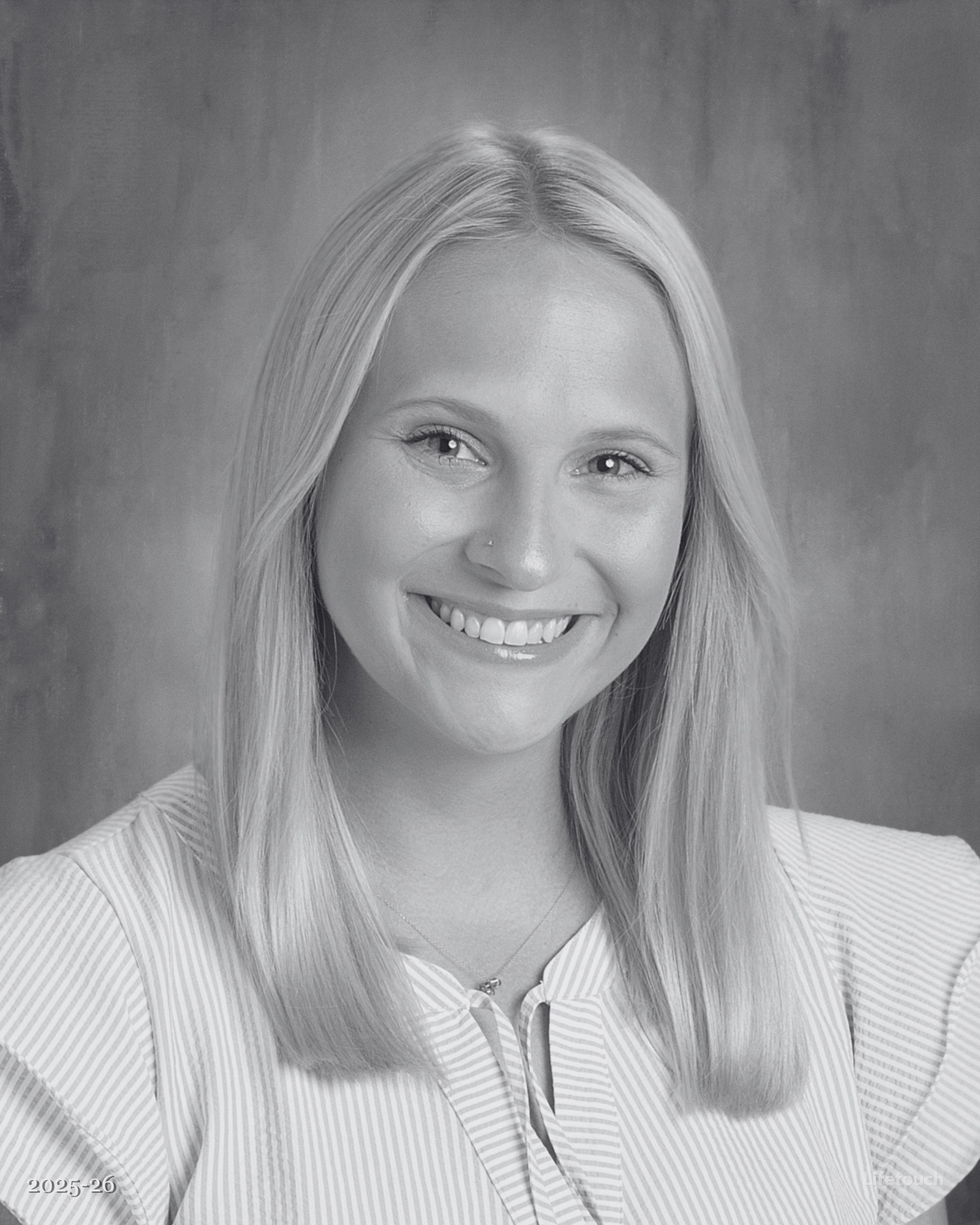 Black-and-white portrait of a young woman with long straight hair, smiling, wearing a collared shirt with a vertical stripe pattern.