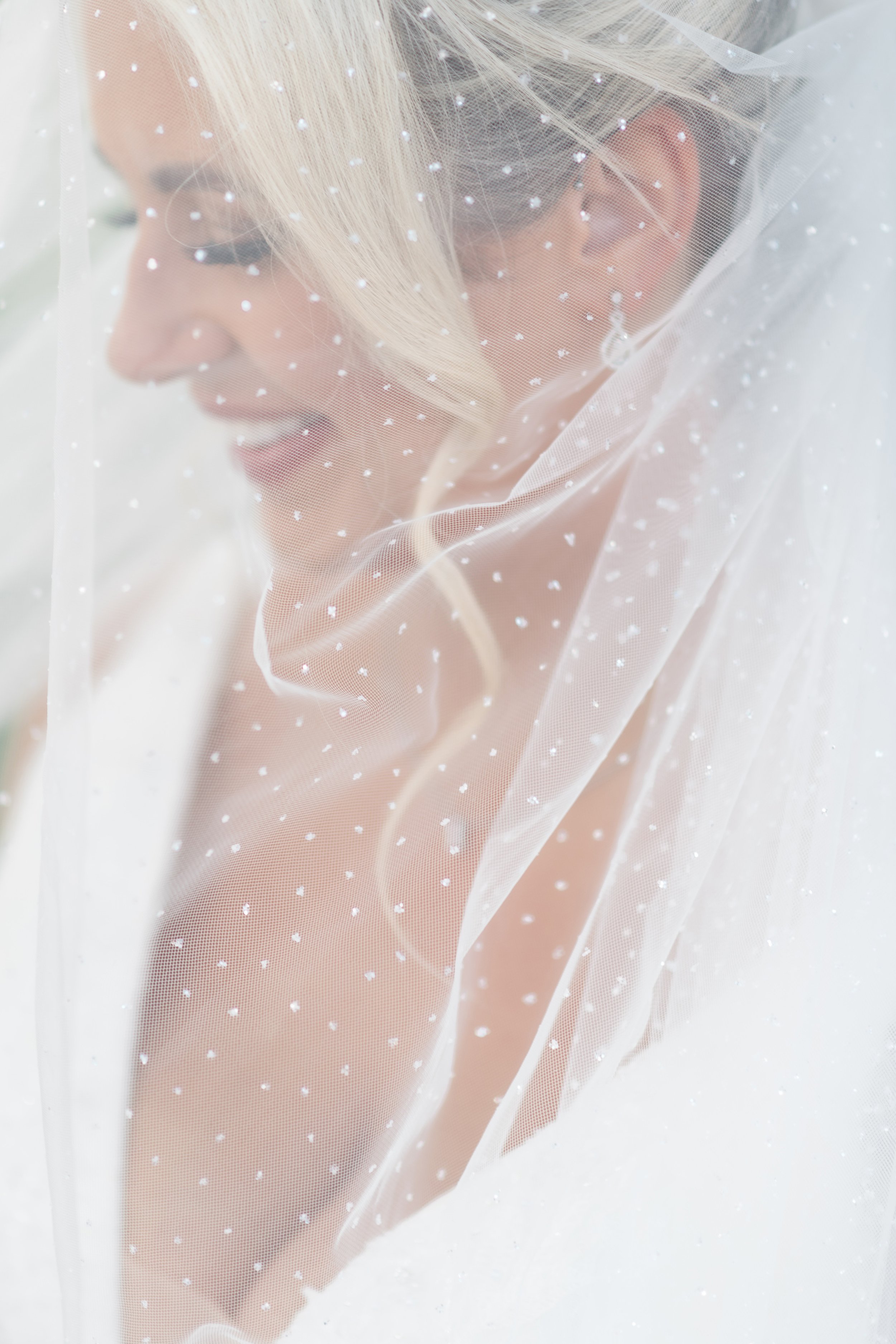 Close-up of a smiling woman with light blonde hair, wearing bridal veil decorated with small pearls.