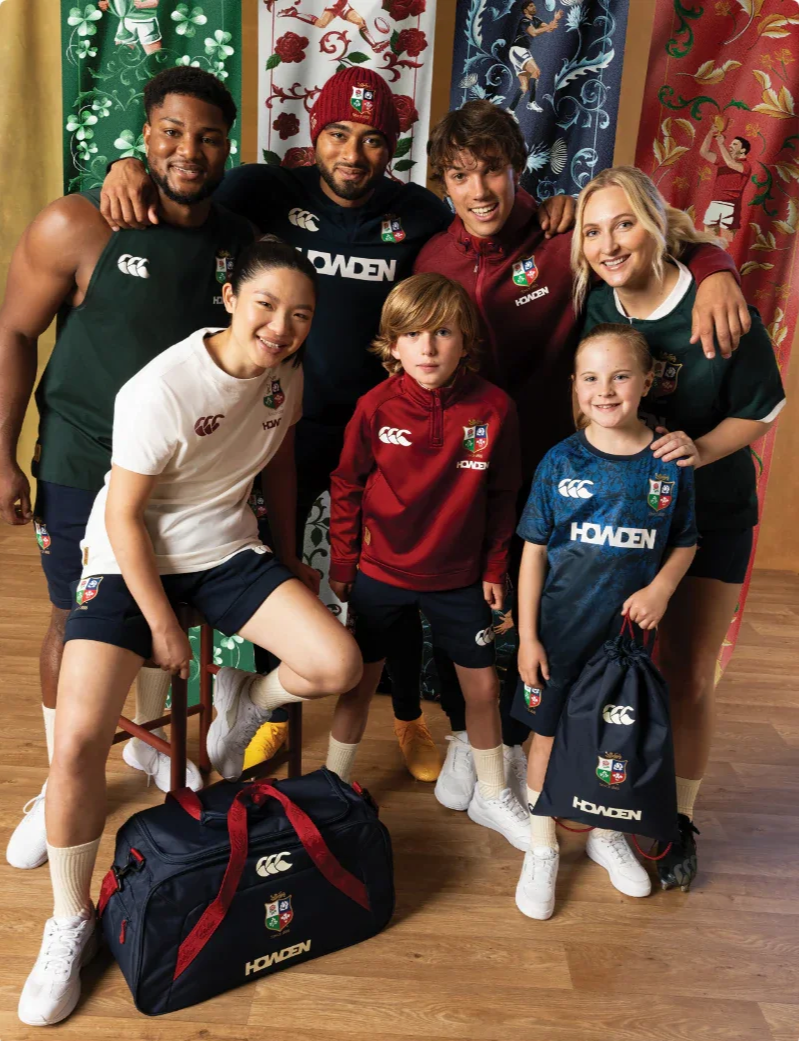 Group of young athletes, six males and two females, wearing sports uniforms with logos and sponsor names, posing together in front of colorful tapestry backgrounds. Some are holding sports bags.