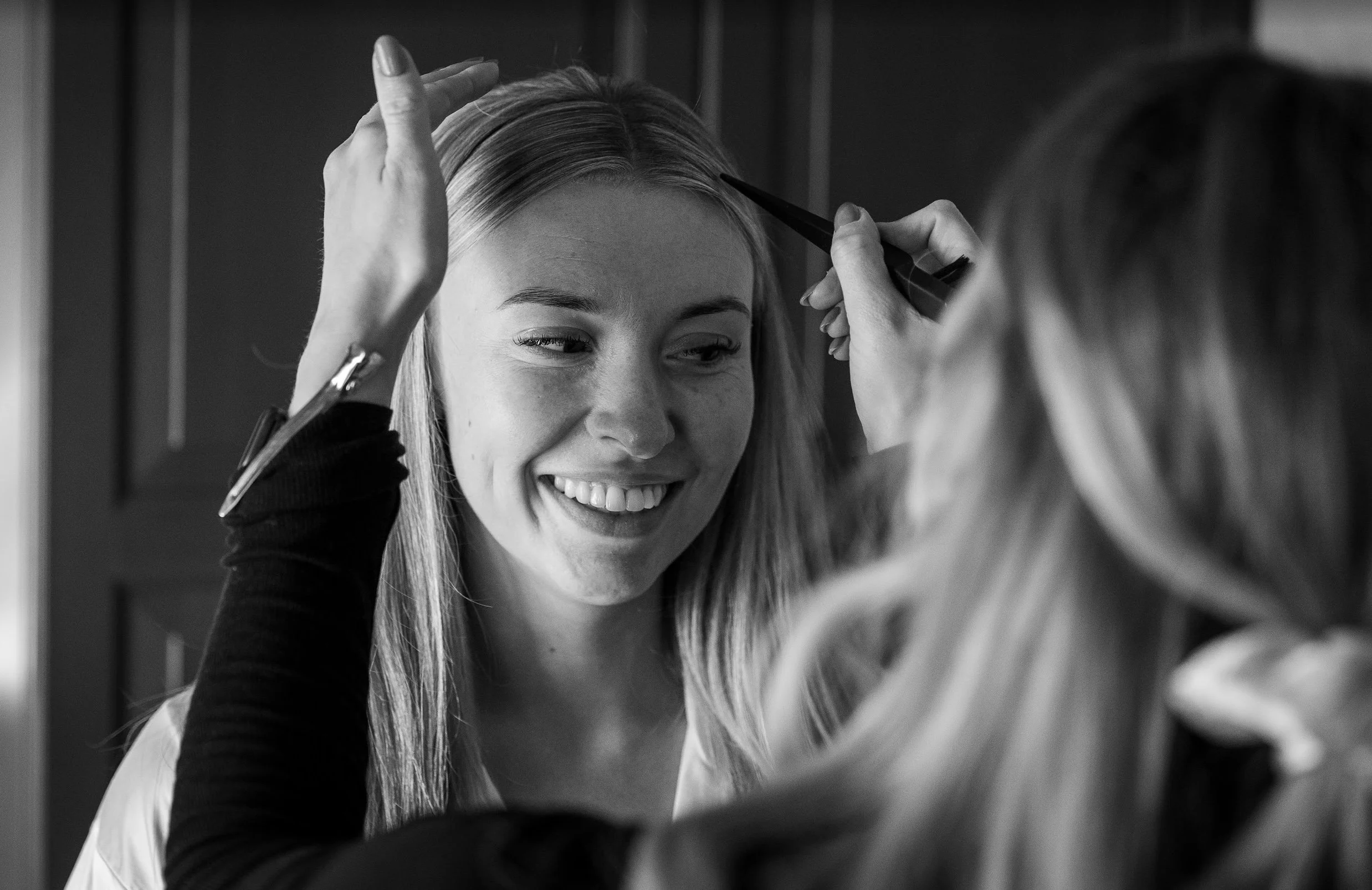A makeup artist applying makeup to a smiling woman with long hair, in a black and white photo.
