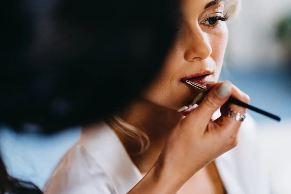 Woman applying lipstick with a makeup brush while looking into a mirror