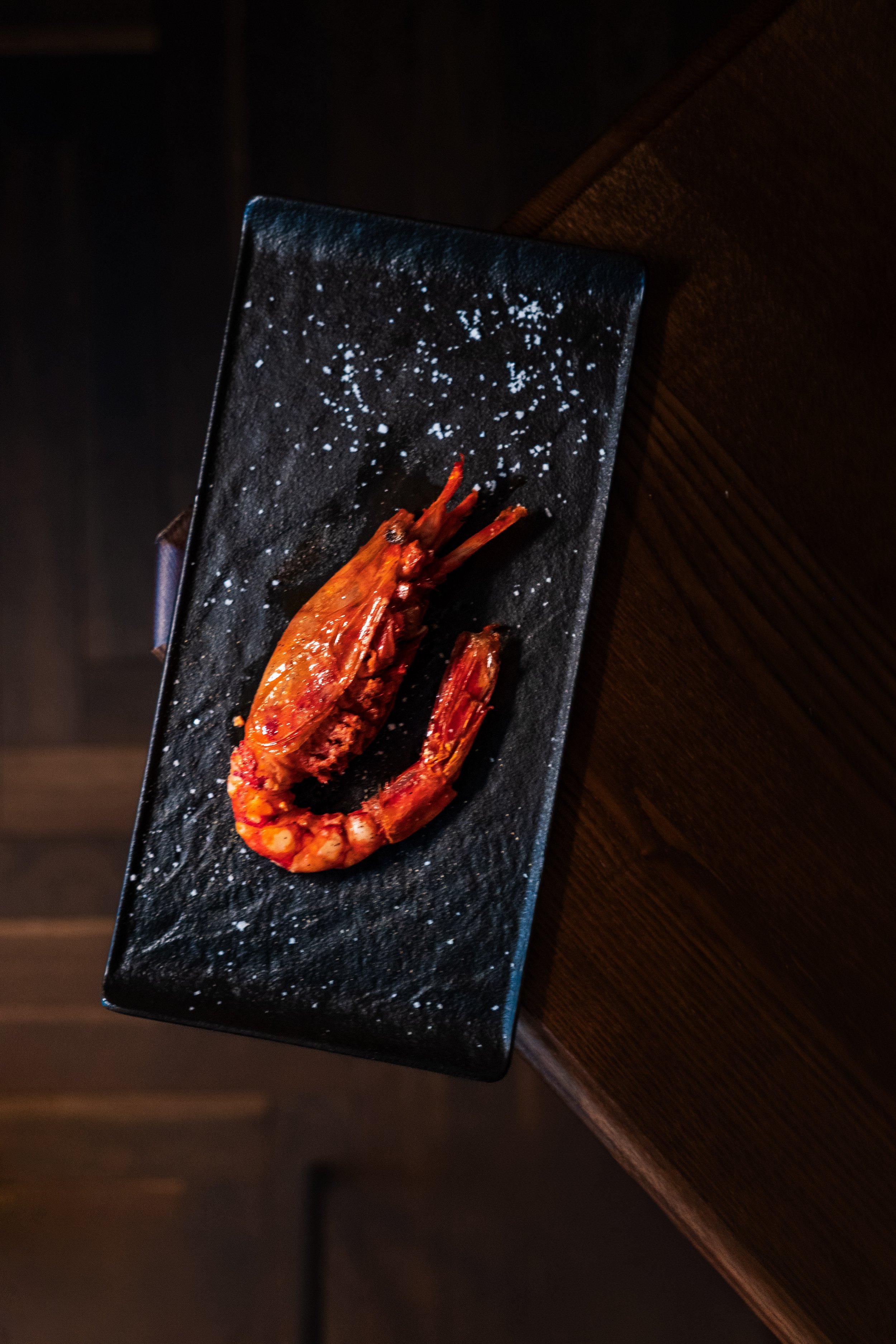 Gambas rouges grillées sur une assiette noire, décorée de sel ou farine.