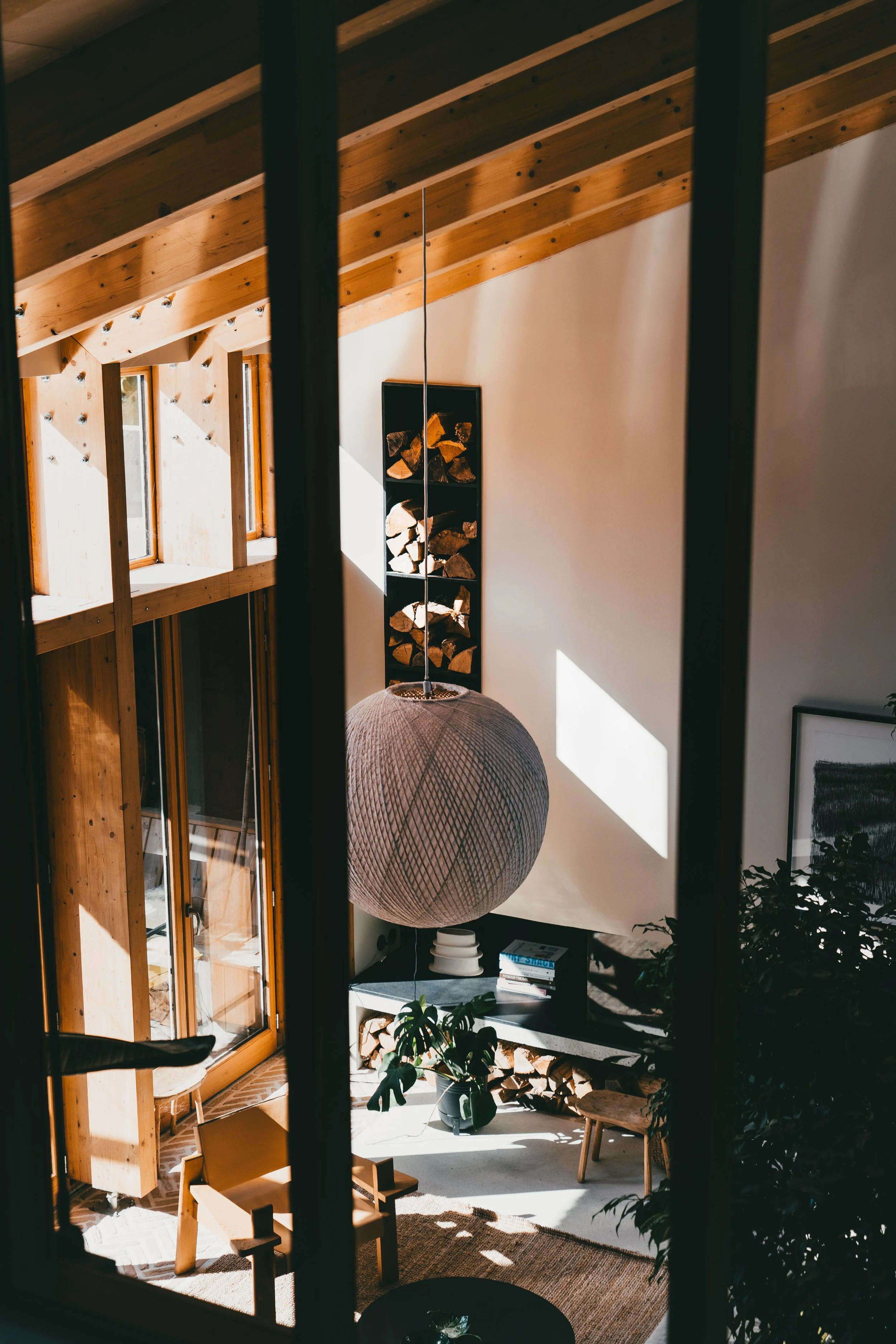 Intérieur d'un salon avec des murs en bois, une grande lampe suspendue et un poêle à bois prêt à être utilisé, avec plusieurs petits meubles et plantes décoratives.