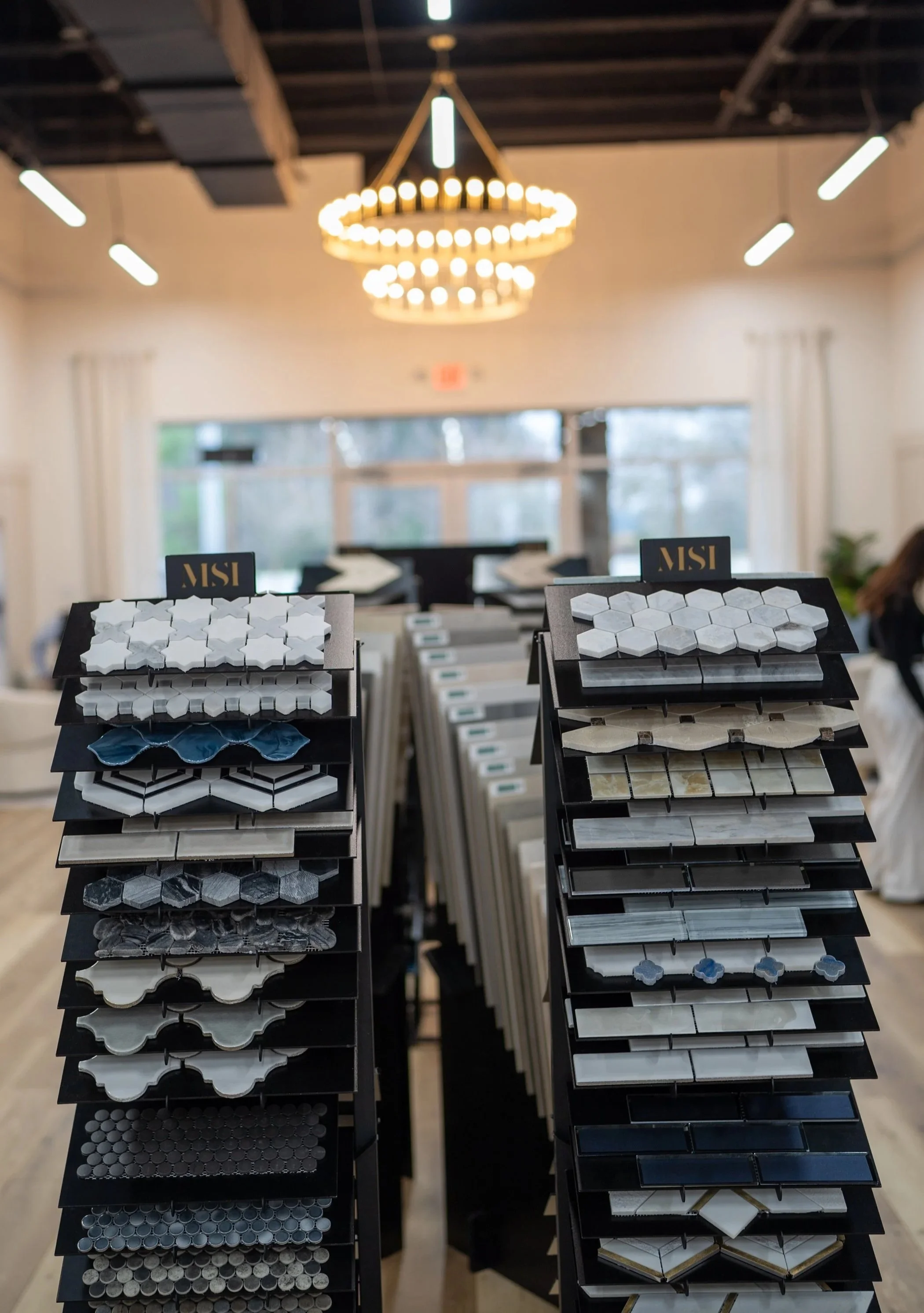Display of various tile samples in a showroom with modern lighting and a chandelier in the background.