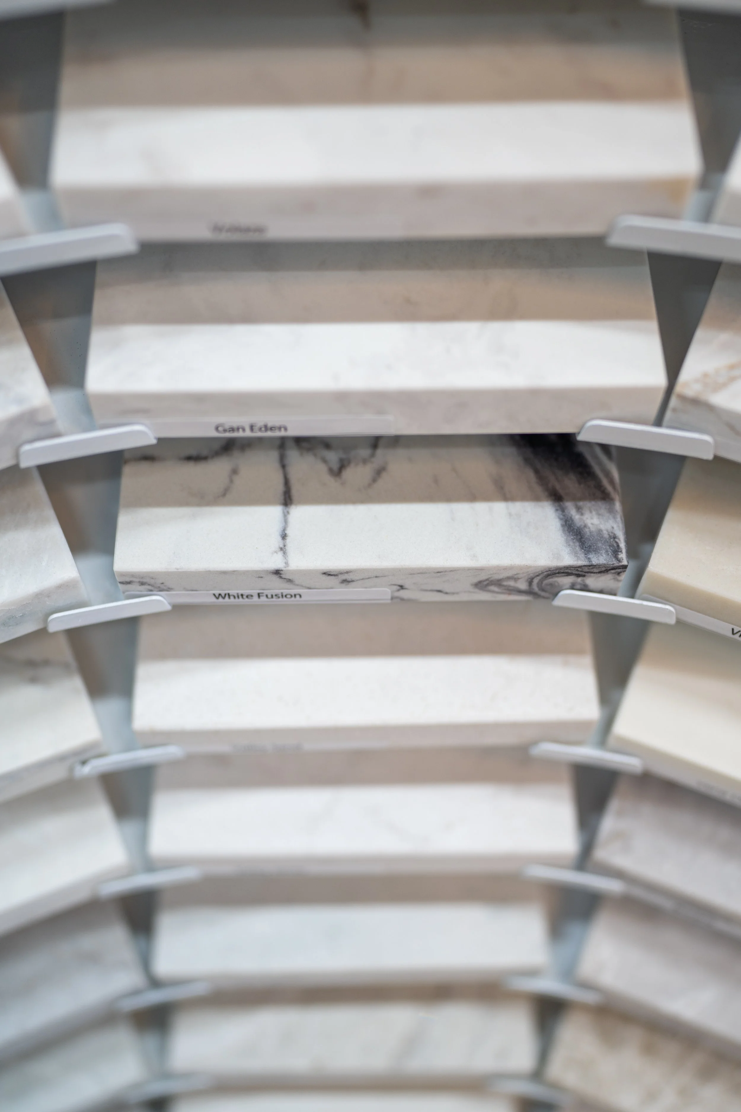 Display of marble countertop samples in various patterns and colors on a rotating stand, with some labeled, such as 'Gan Eden' and 'White Fusion' at Seamless Floors showroom located in St Augustine