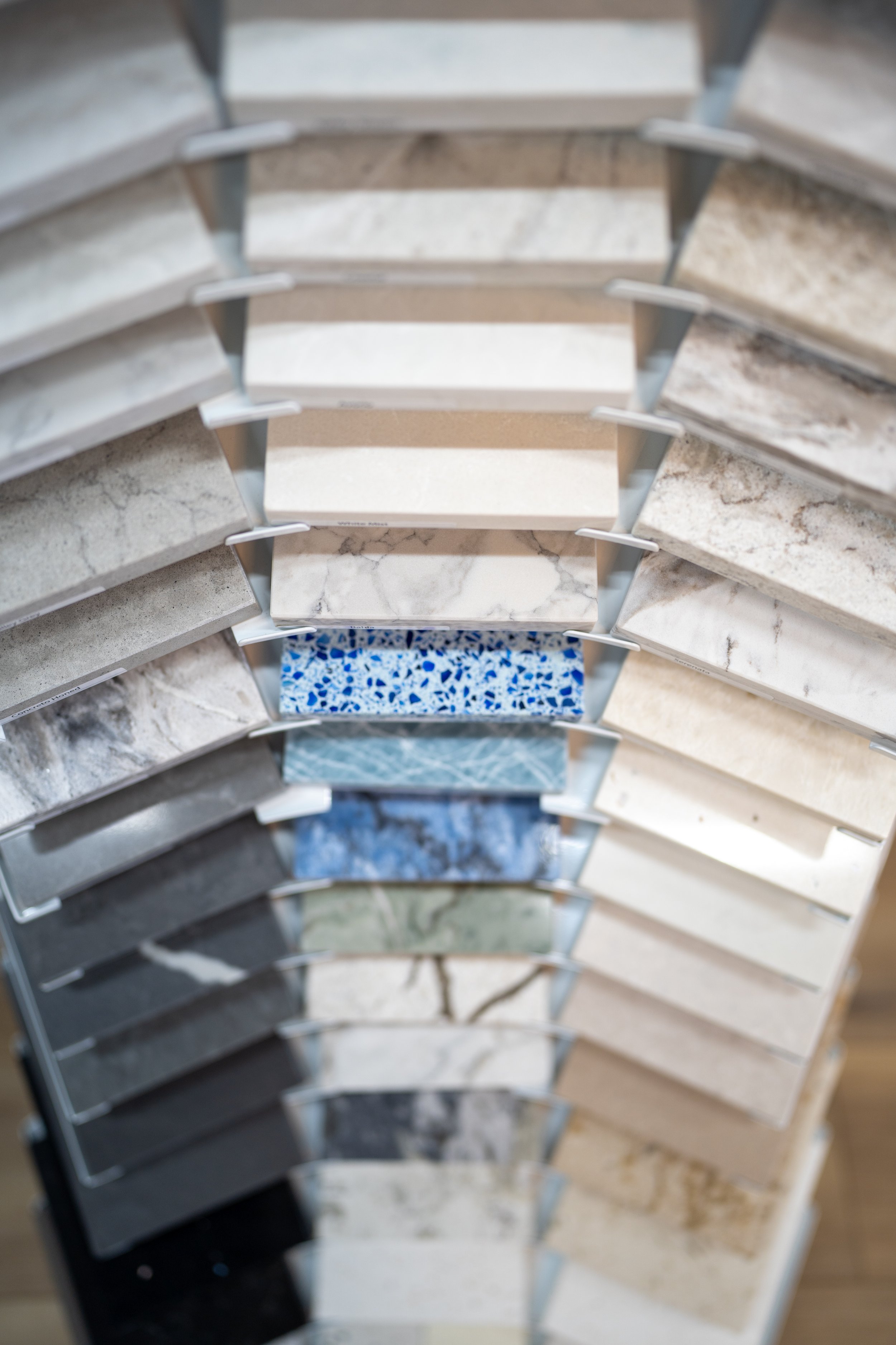 A colorful display of various marble and stone samples arranged in a tiered rack, showcasing different patterns and colors at Seamless Floors showroom located in St Augustine.
