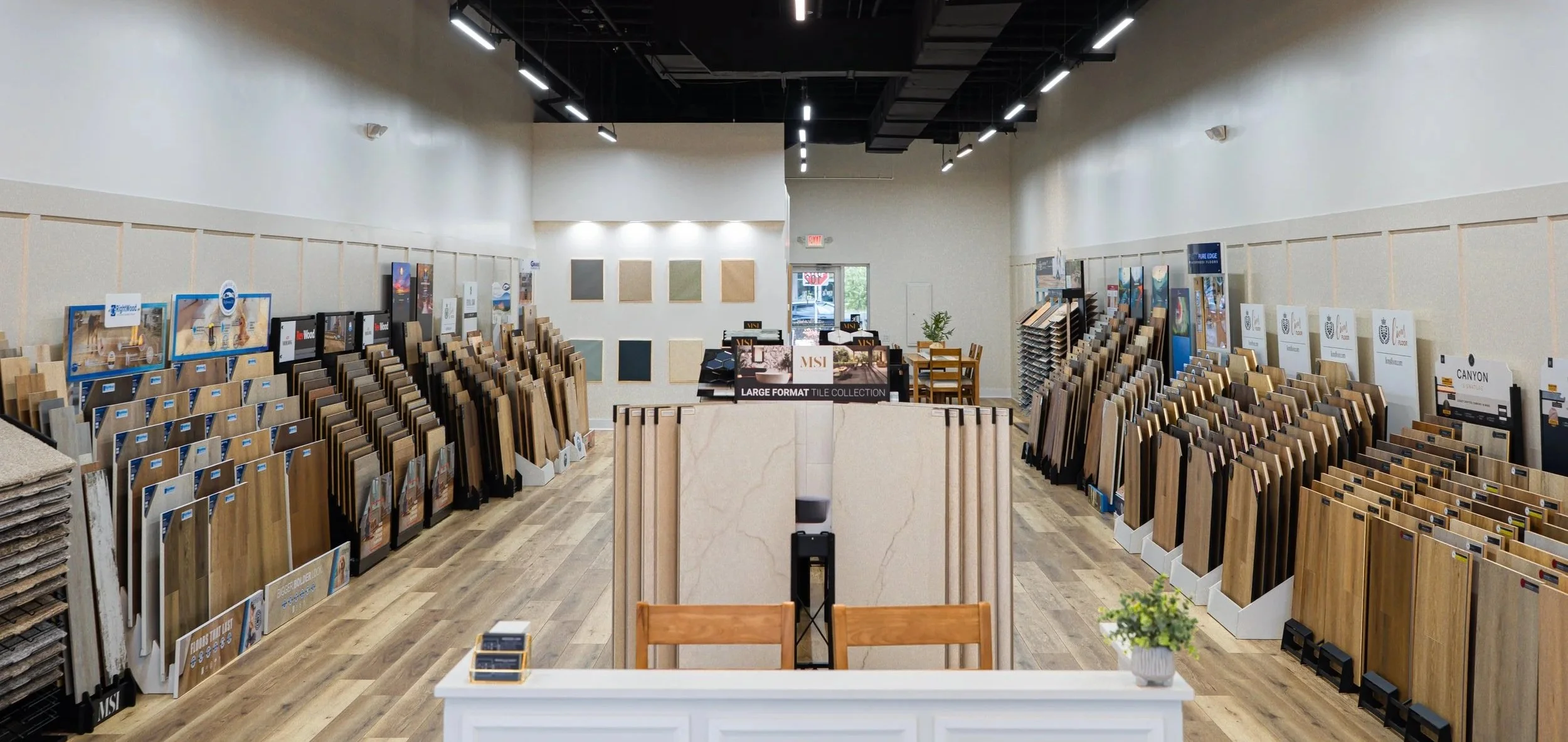 Interior of a Seamless Floors, a St Augustine flooring store with display racks of wooden flooring samples on both sides and a center display with large format tiles.