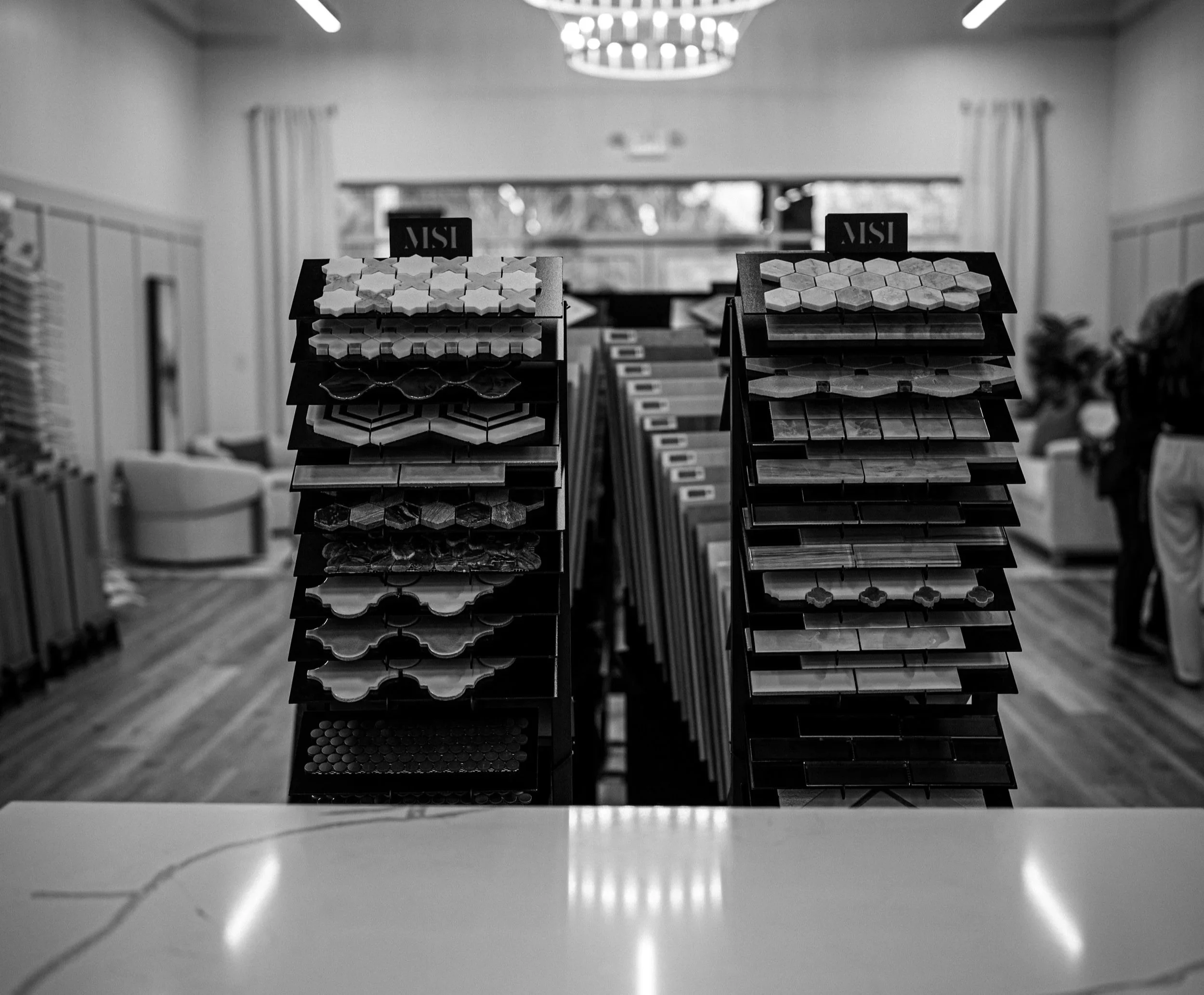 Display racks filled with various tiles in a store with people in the background.