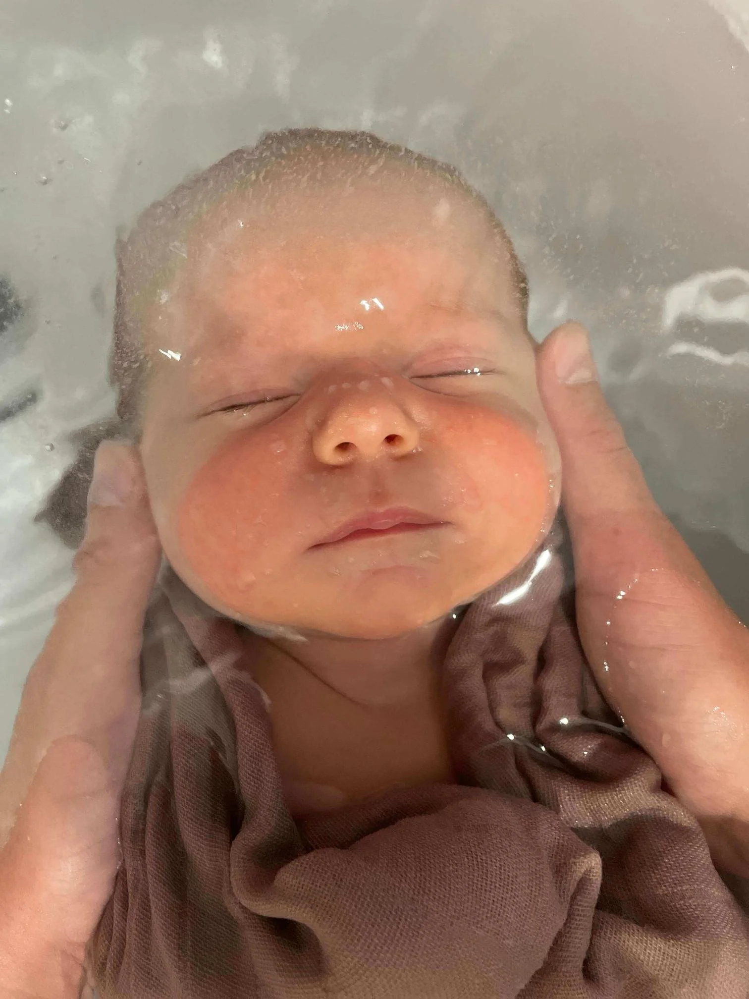 Un bébé qui prend un bain, avec une personne qui soutient doucement sa tête sous l'eau.