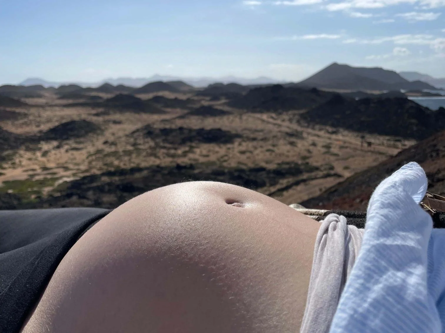 Vue d'un paysage désertique avec des montagnes, prise depuis une position allongée avec un ventre de femme enceinte au premier plan