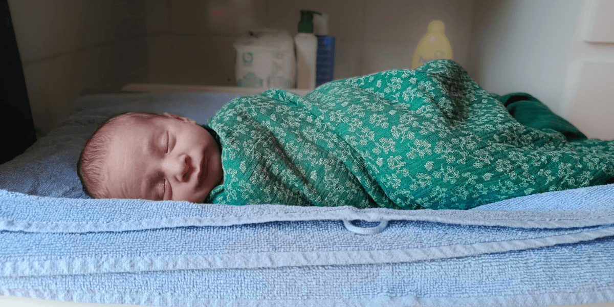 Un bébé emmailloté avant d’aller dans le bain, enfant apaisé quasiment endormi.
