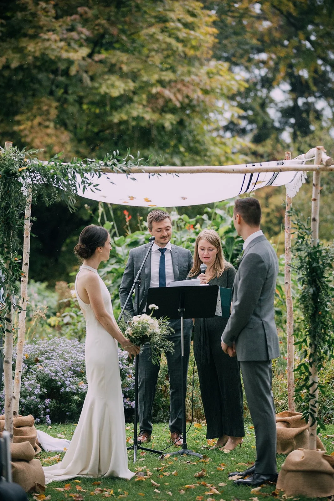 A bride and groom stand in front of a arbor on their wedding day