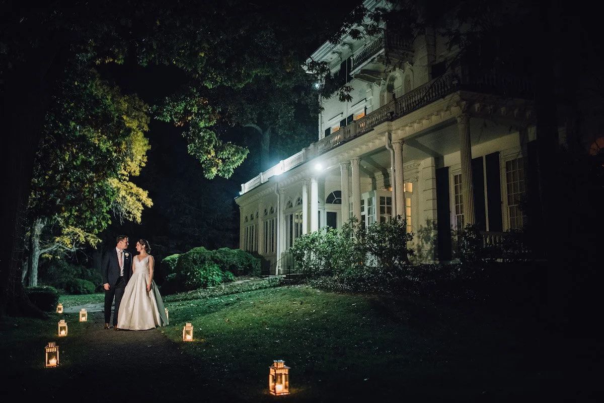A bride and groom stand outside a mansion