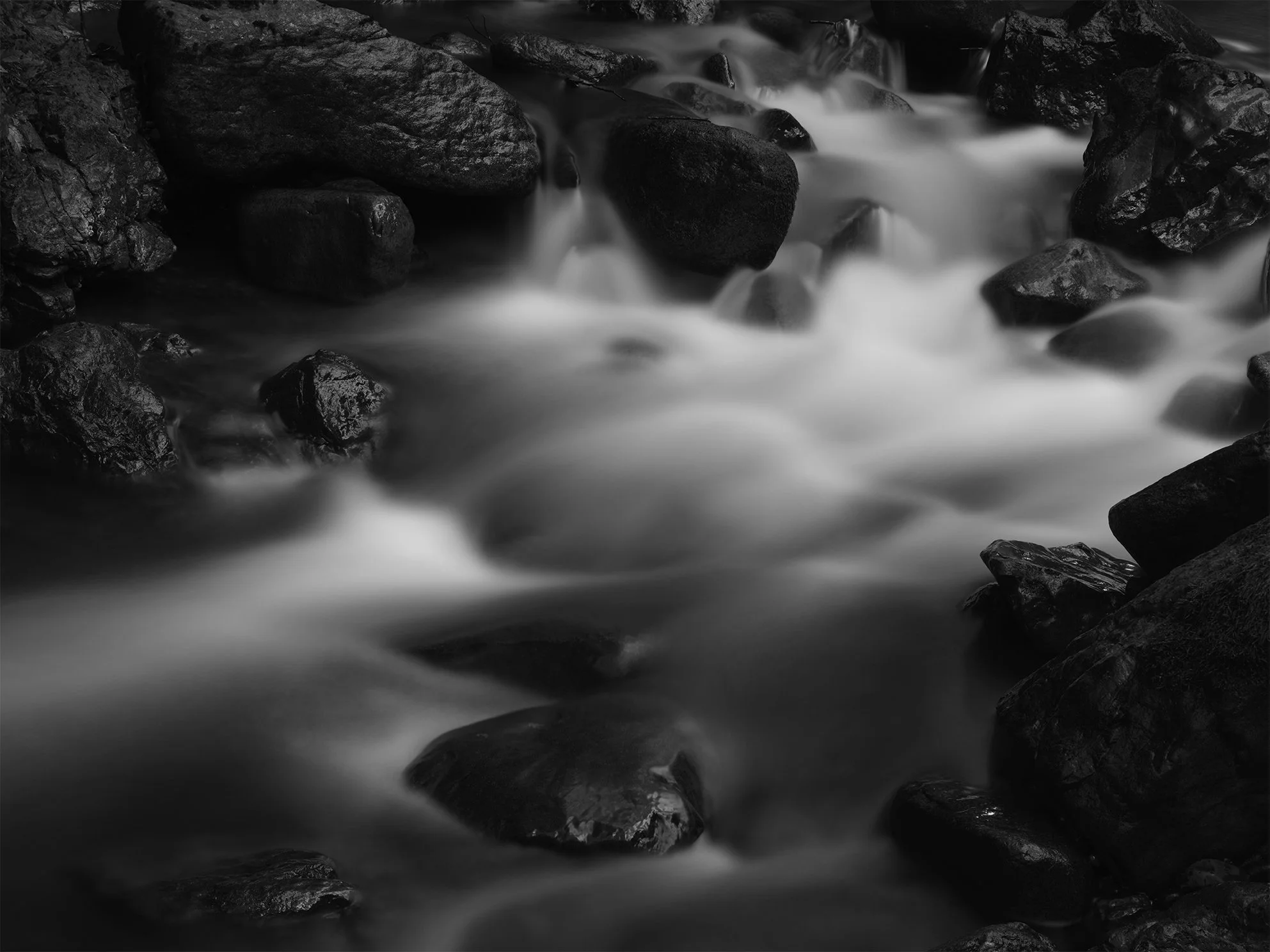 Black and white photo of water flowing over and around rocks in a stream or river.