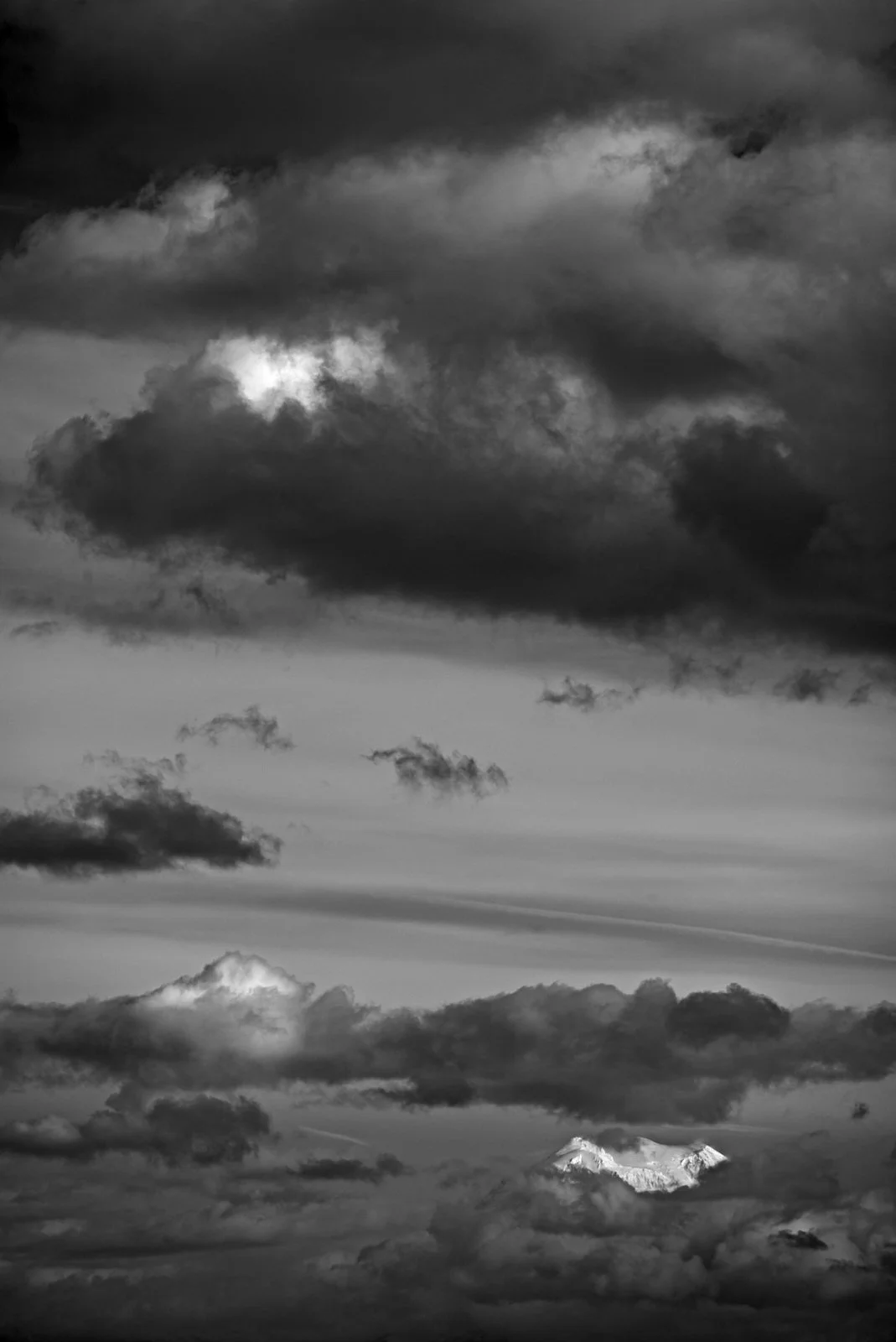 Black and white photo of a cloudy sky with a mountain peak in the distance.