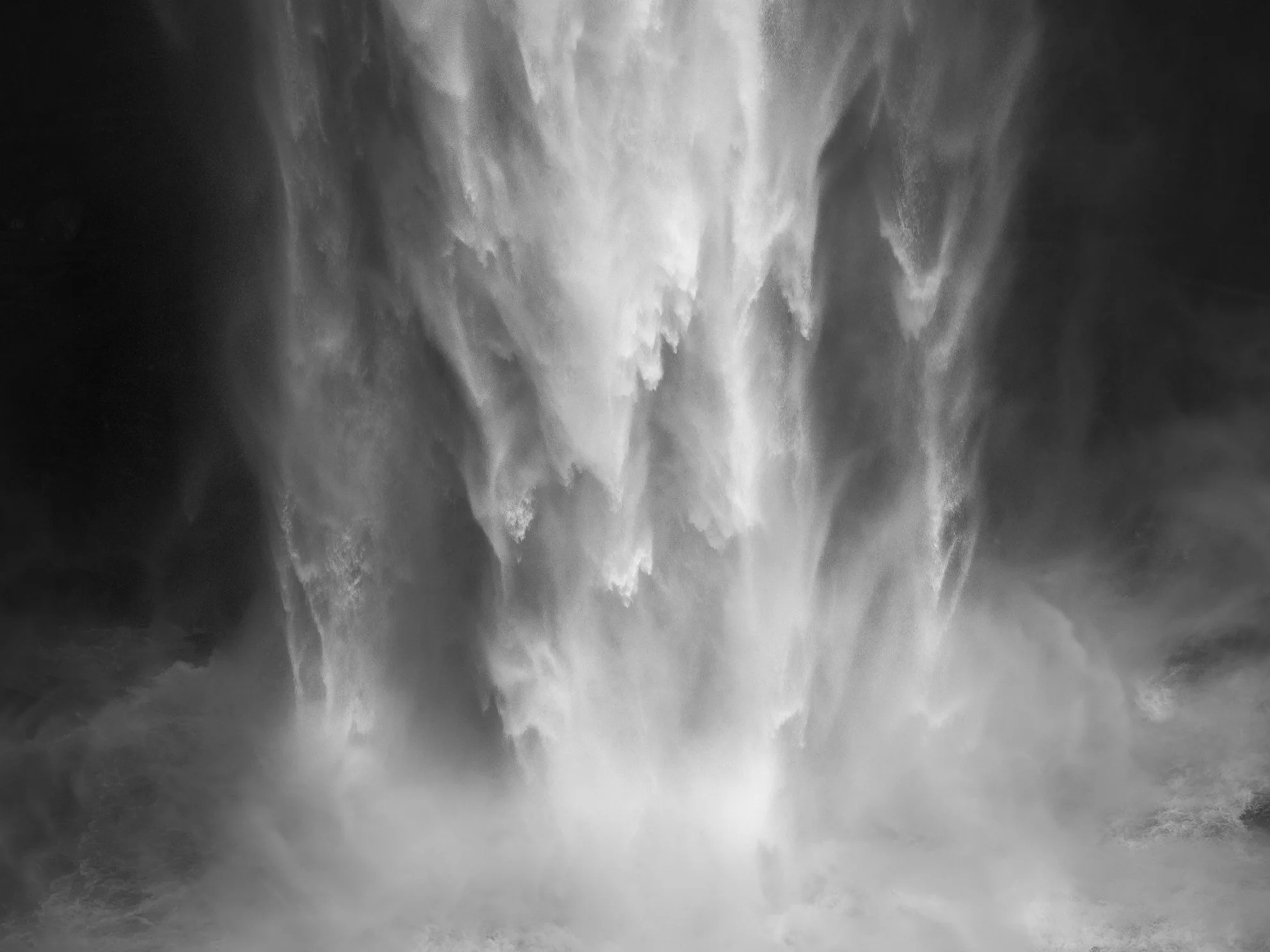 A black and white image of a waterfall with water cascading down rocks and mist forming at the base.