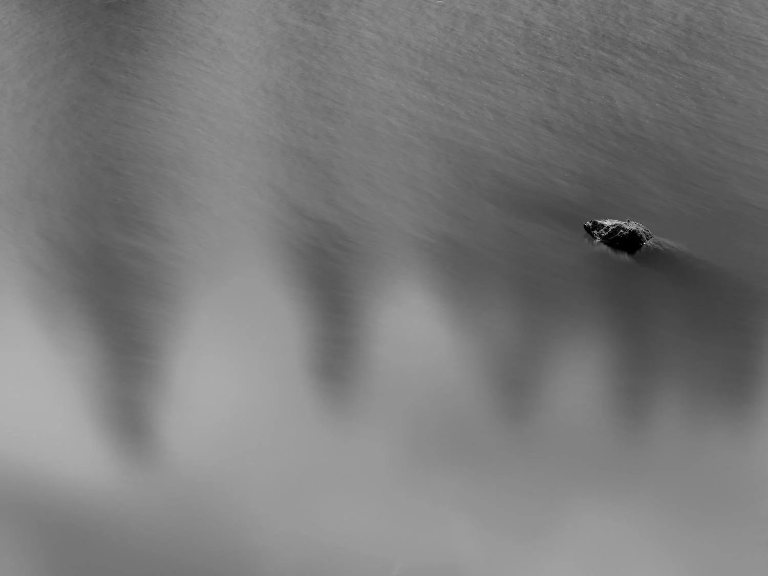 Black rock in water with blurred surface, black-and-white photo.