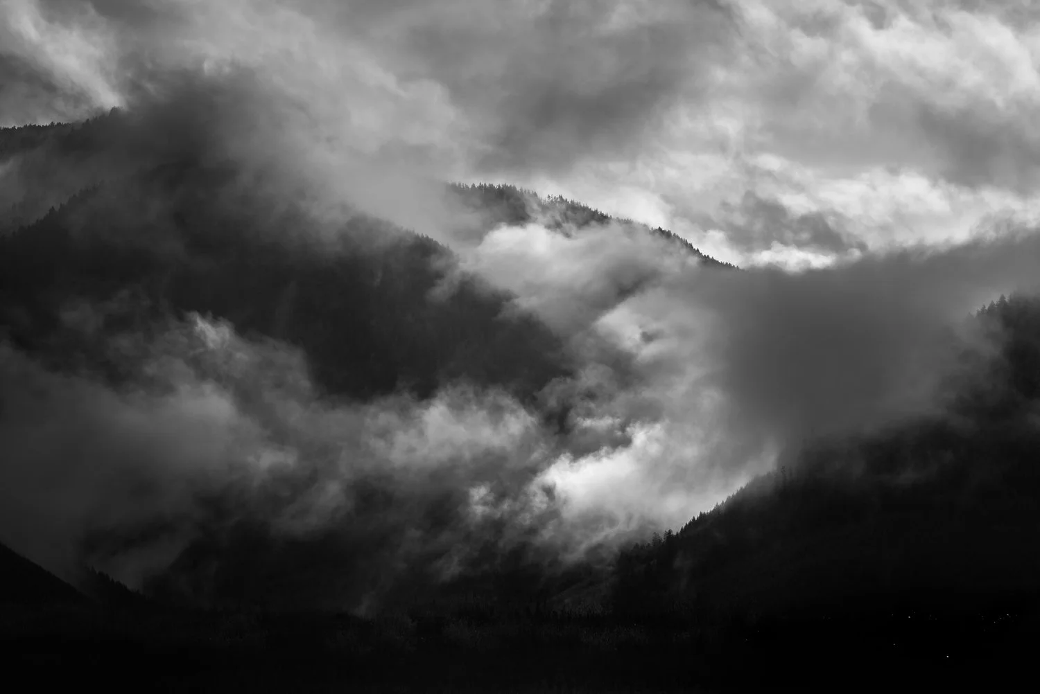 Black and white photograph of a mountain landscape with fog and clouds covering the peaks and valleys.