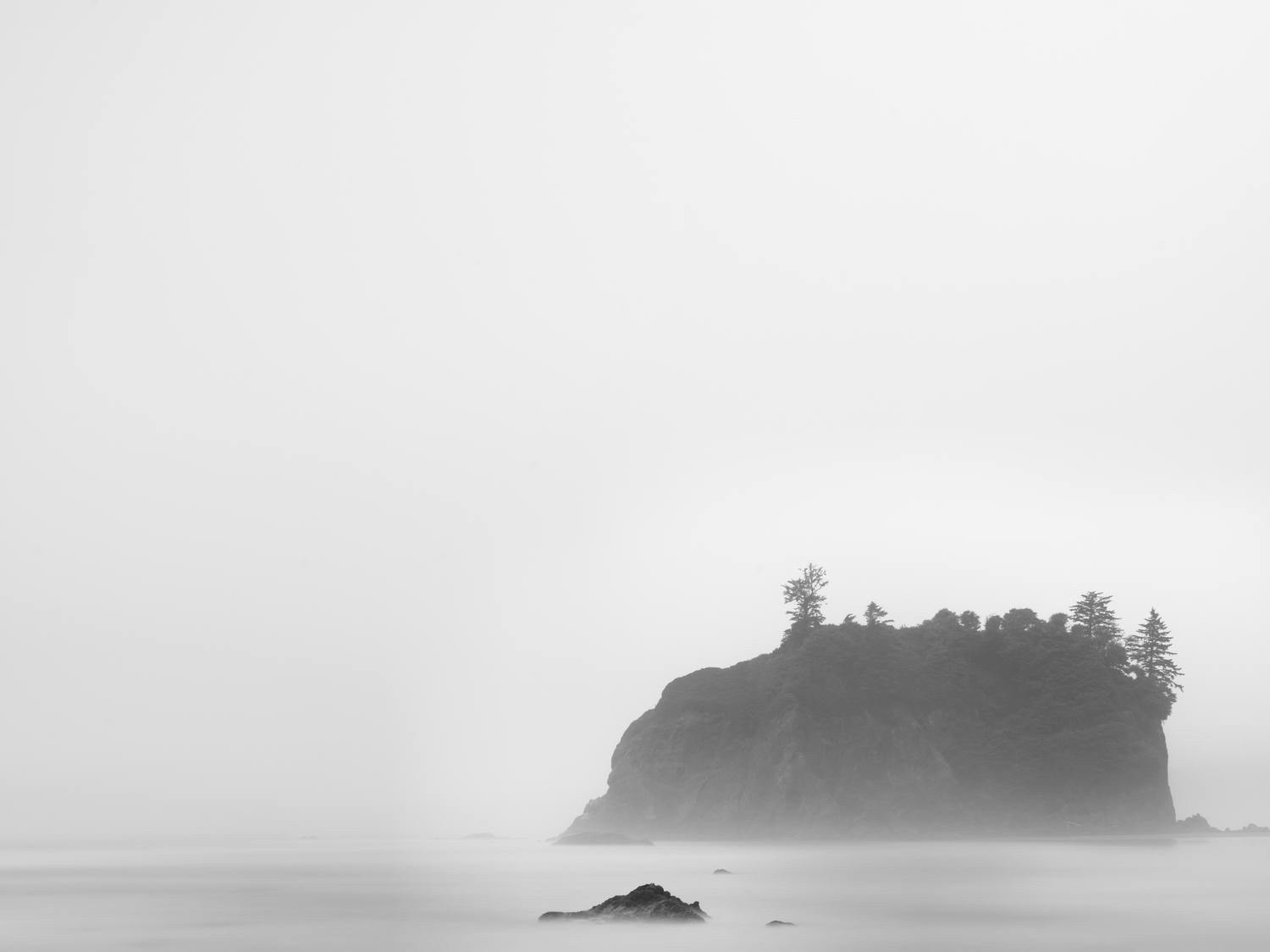 A foggy seascape with a large rocky island covered in trees.