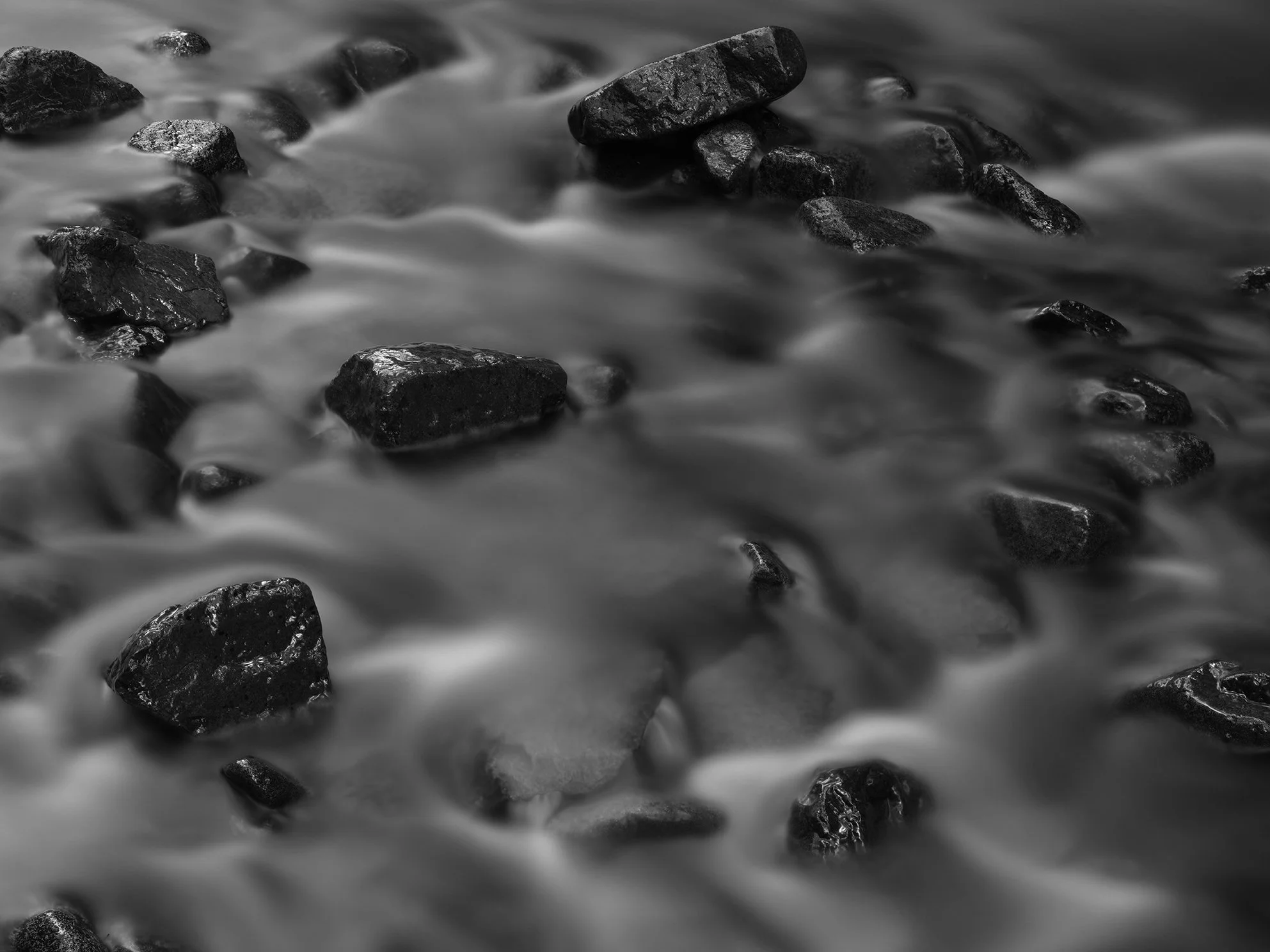 Black and white photo of rocks in water with a long exposure effect.