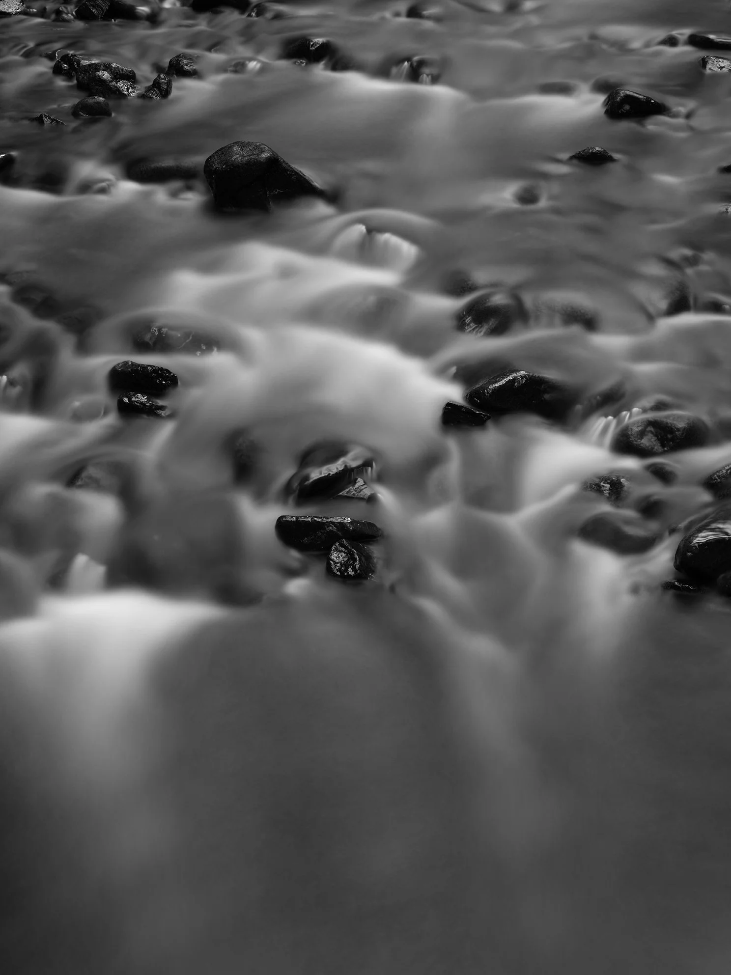 Black and white long exposure photograph of water flowing over rocks in a river or stream.