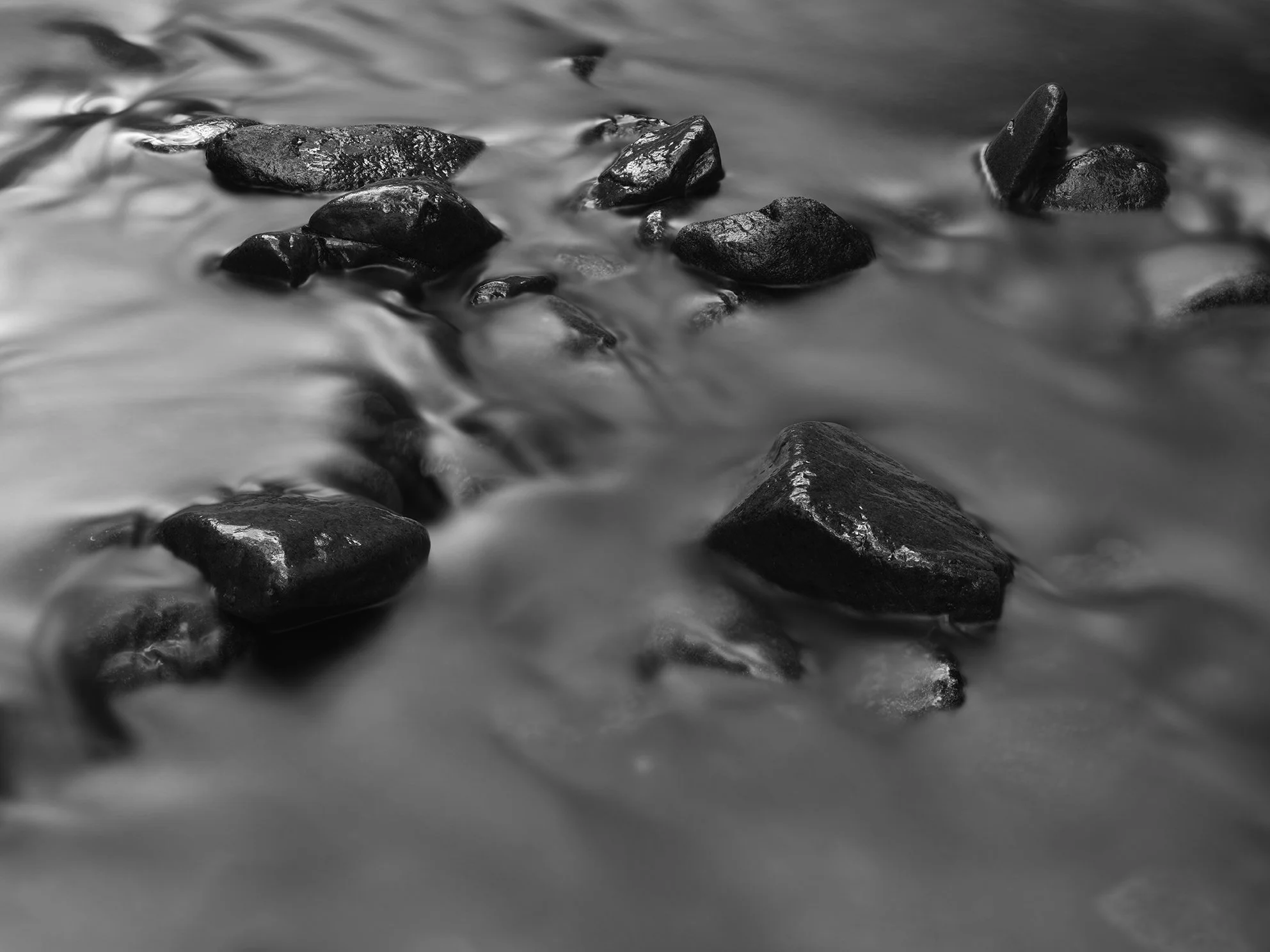 Black rocks partially submerged in water with a long exposure creating a smooth water effect, in black and white.