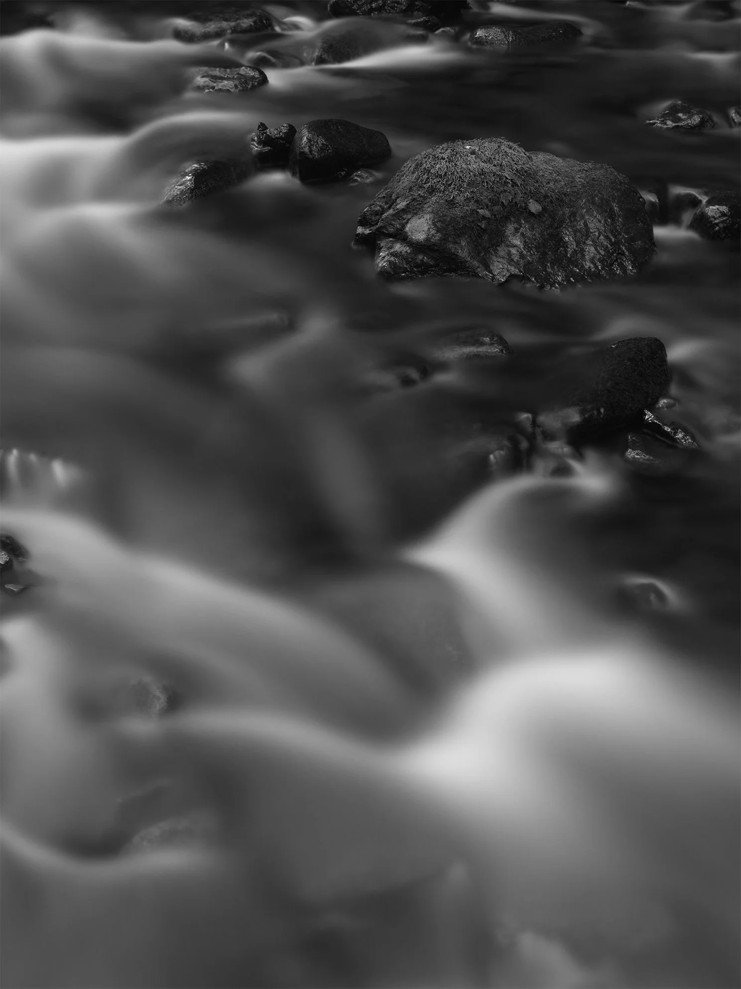 Black and white photograph of rocks in a flowing stream with blurred motion of the water.