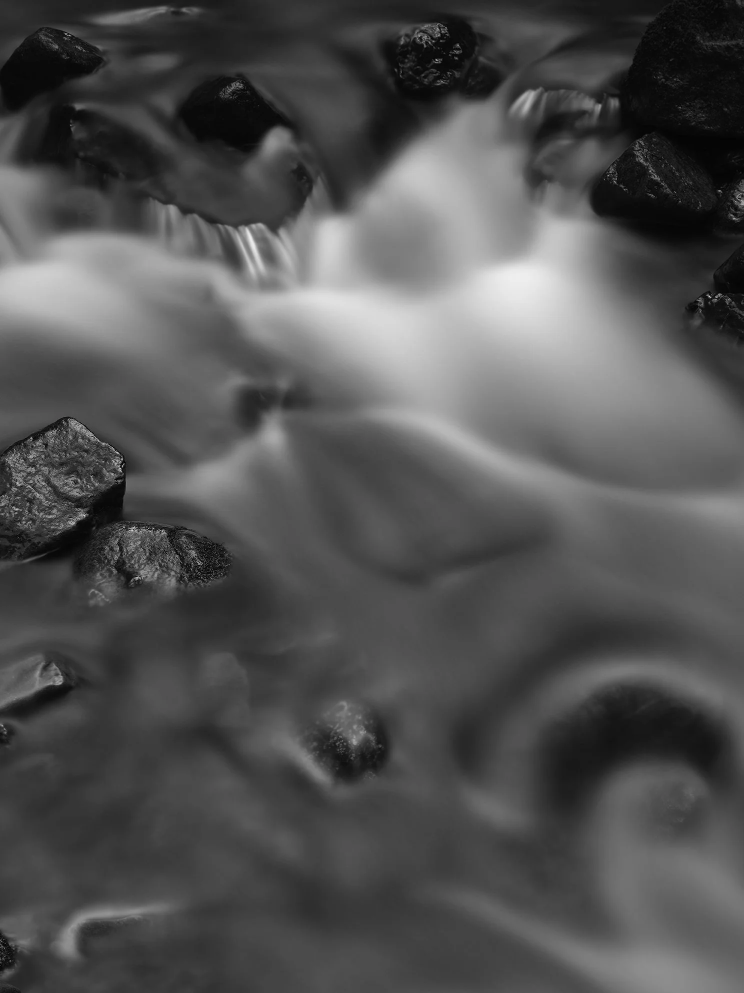 Long exposure black and white photo of water flowing over dark rocks in a river or stream.