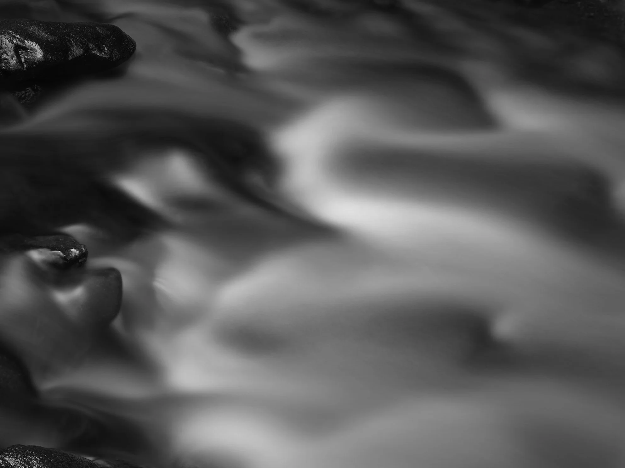 Black and white long-exposure photograph of flowing water over rocks.
