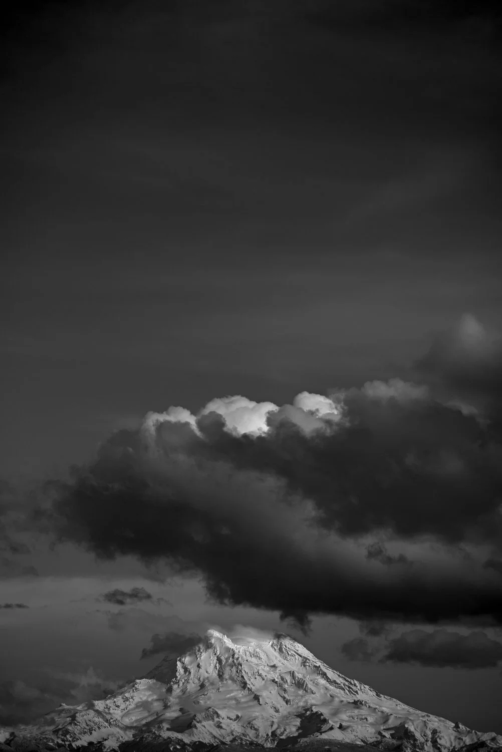 Snow-capped mountain under cloudy sky, black and white photograph.