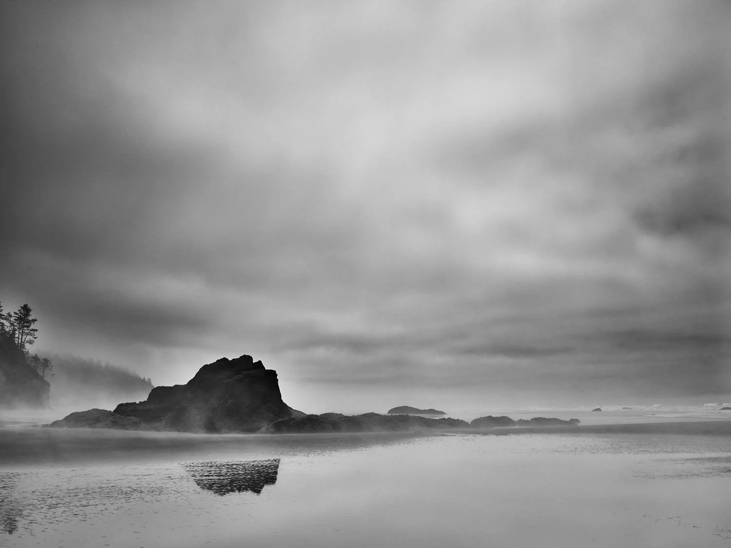 Black and white landscape photo of a rocky island in the ocean with mist and overcast sky.