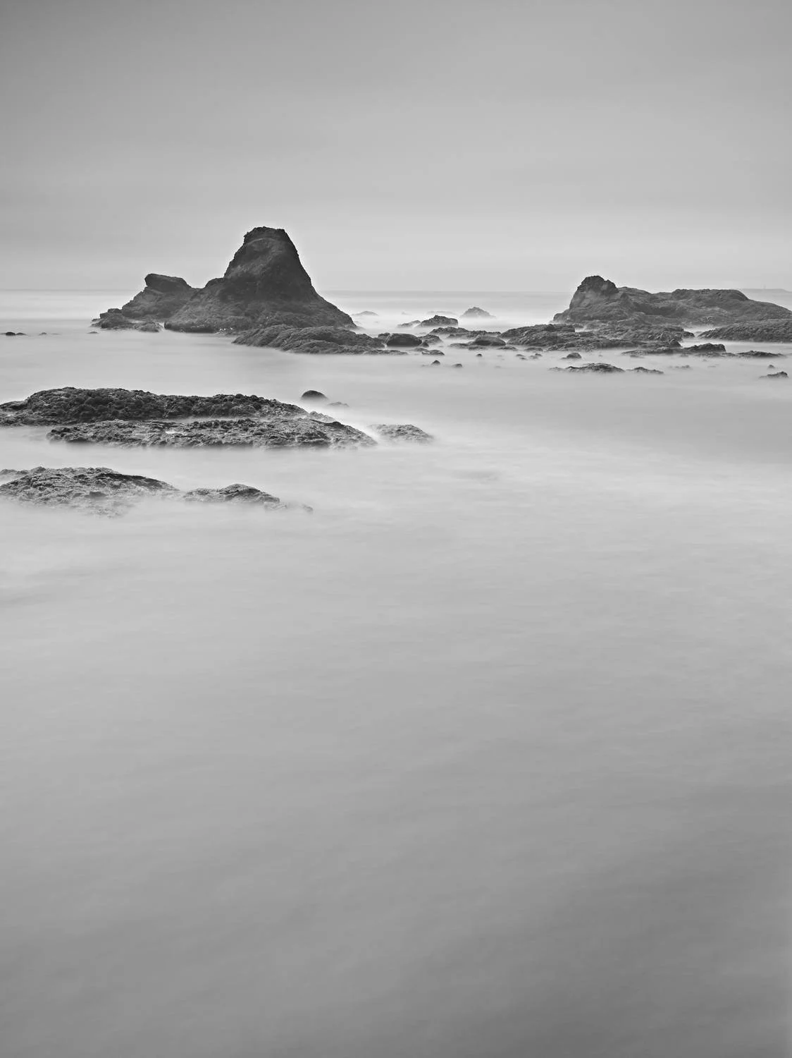 Black and white photo of ocean waves around rocks and small islands