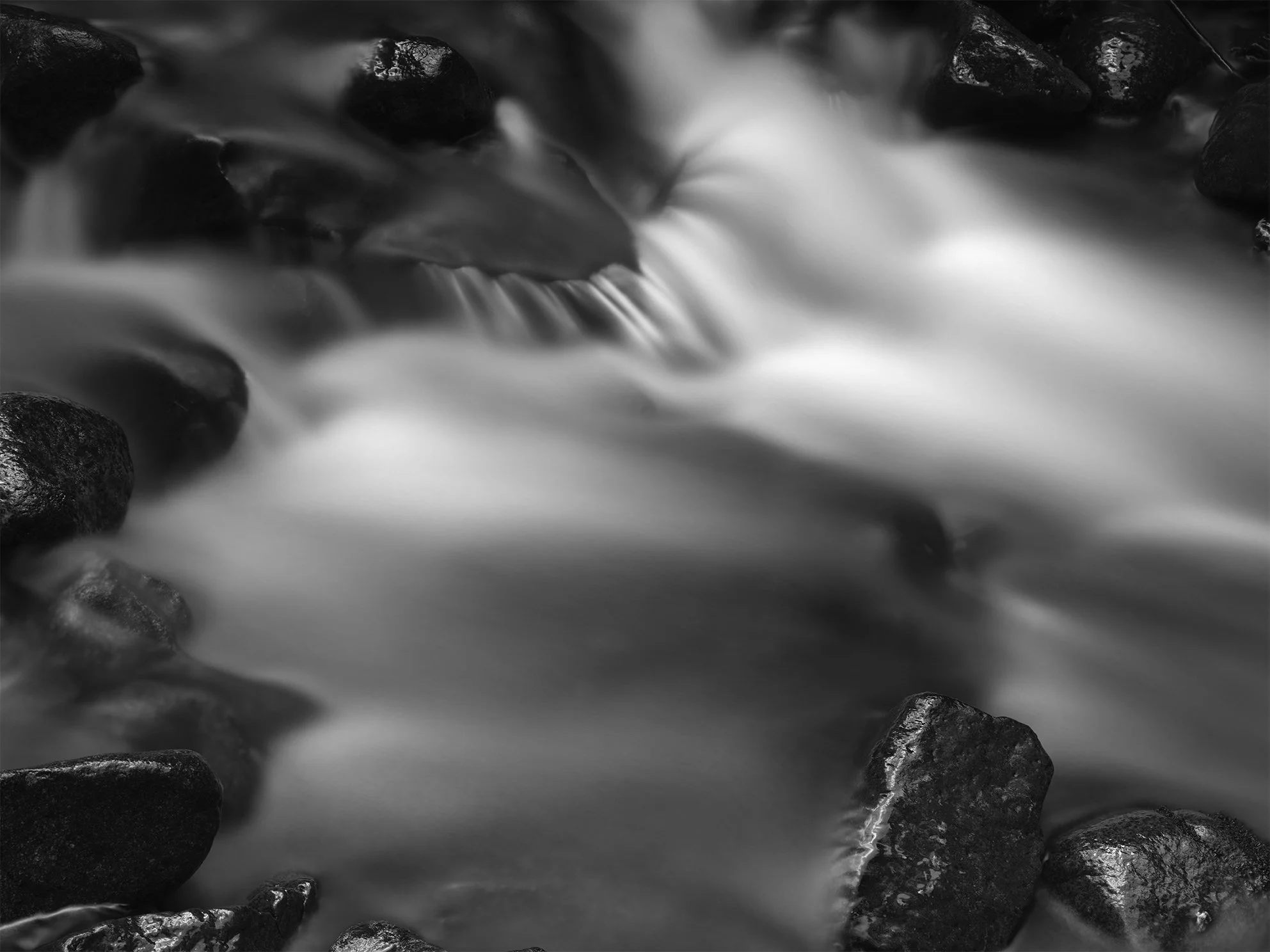 Black and white photograph of water flowing over smooth rocks in a creek or river.