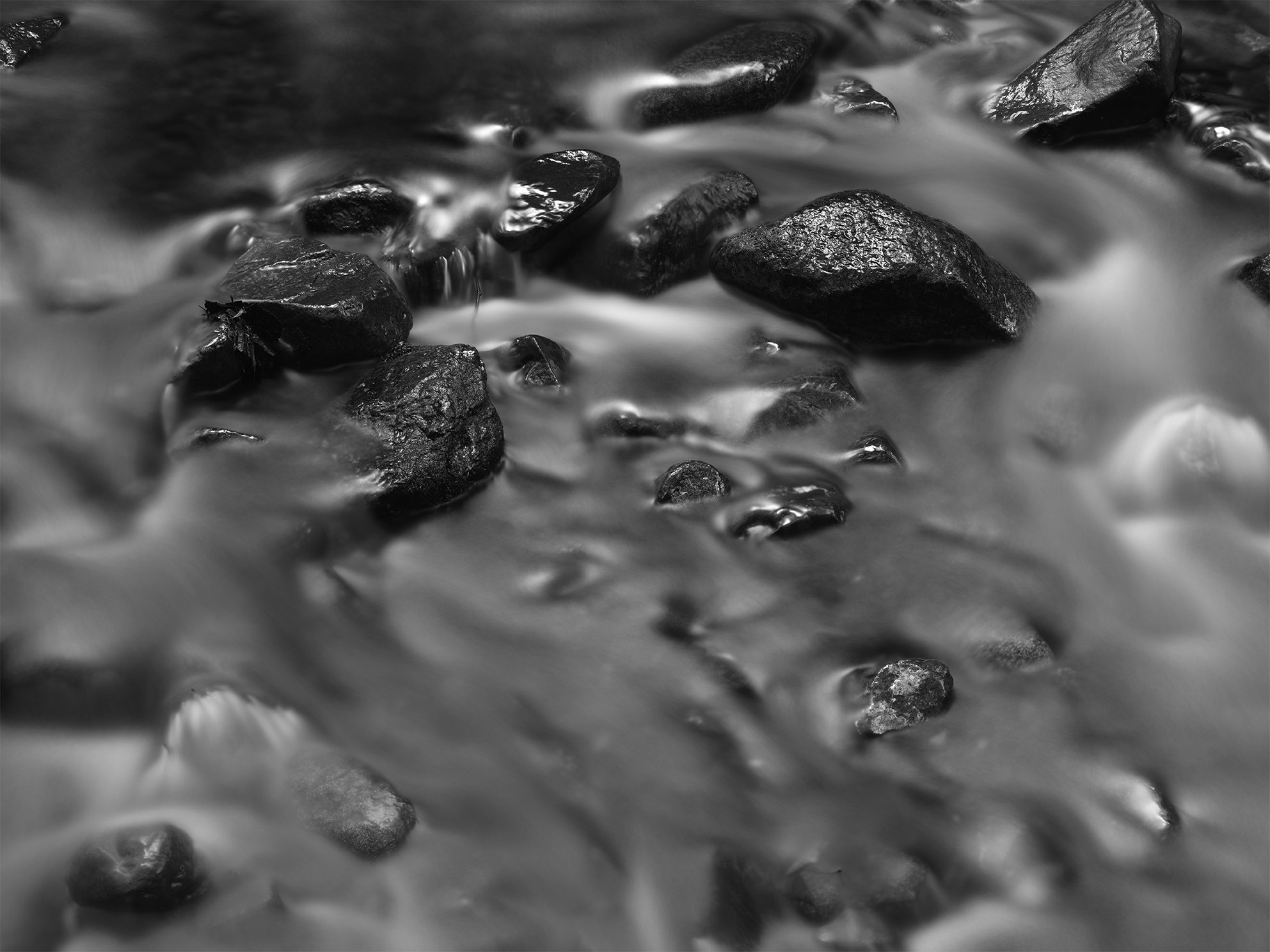Black and white photo of water flowing over rocks in a stream.