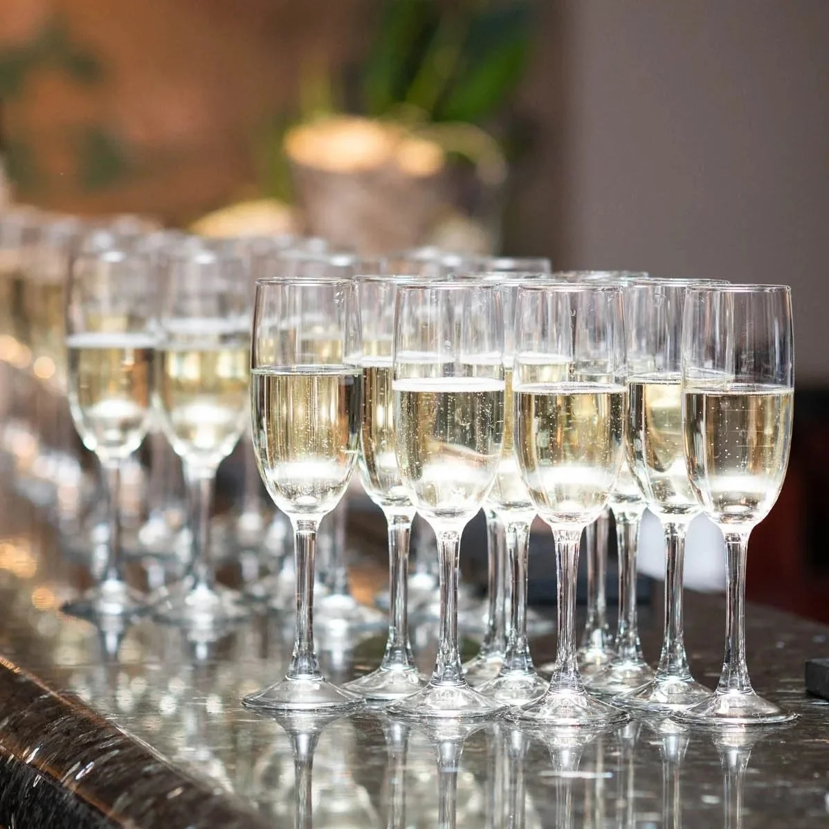 Multiple champagne flutes filled with sparkling wine on a reflective surface.