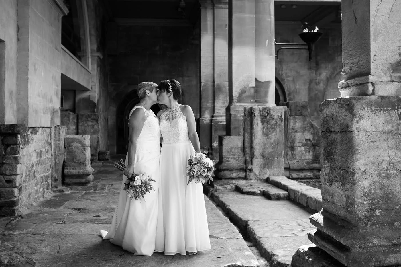 Two brides kissing at their wedding ceremony at the Roman Baths