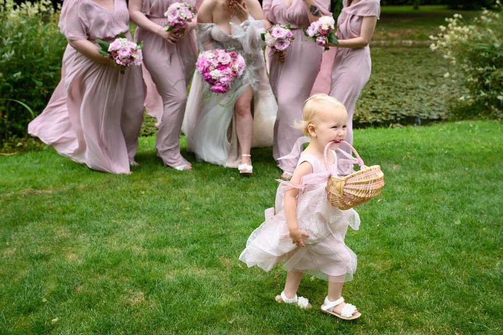 Flower girl walking past bridesmaids with basket in her mouth