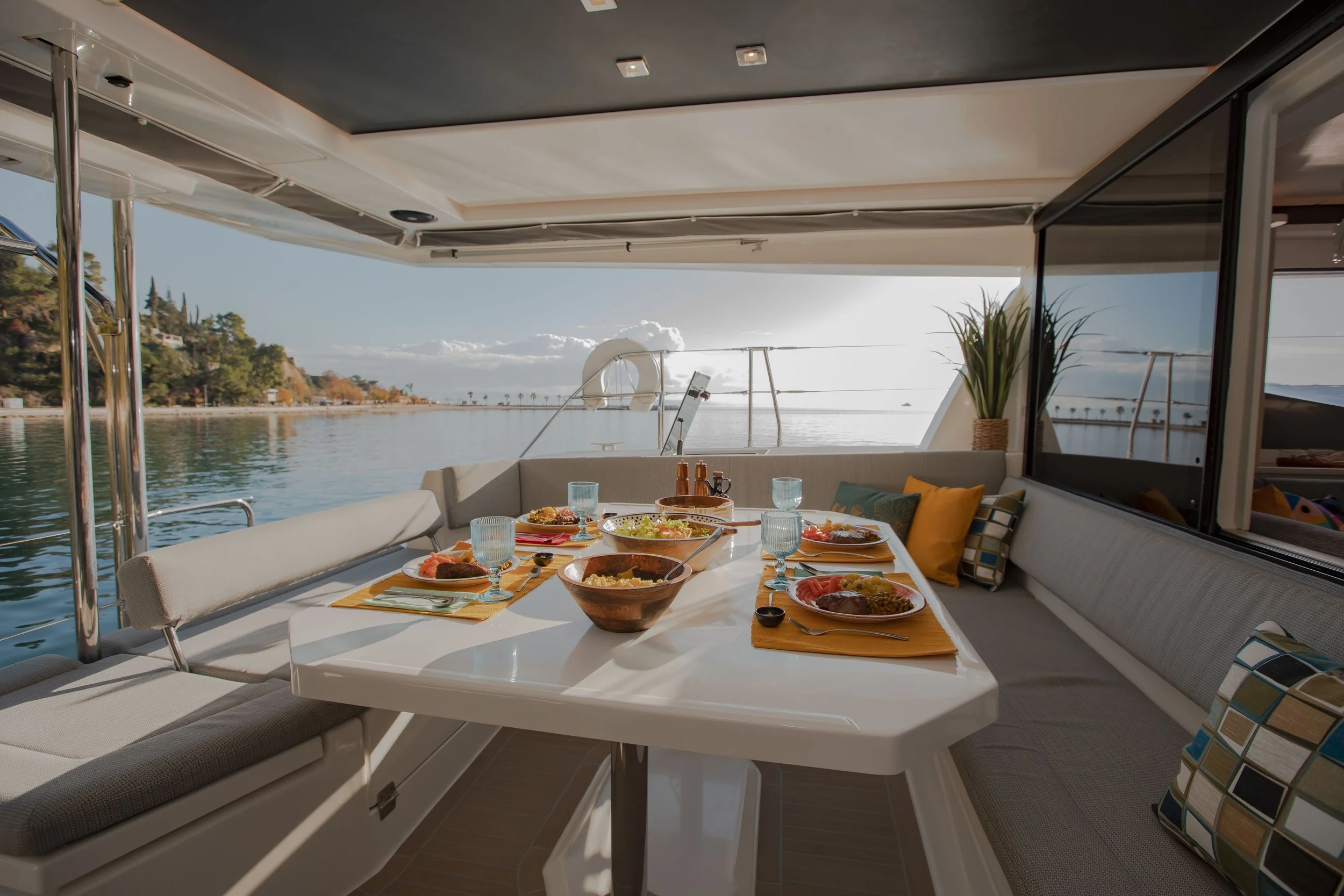 A dining table set for a meal on a yacht with a water view and a coastline in the background.