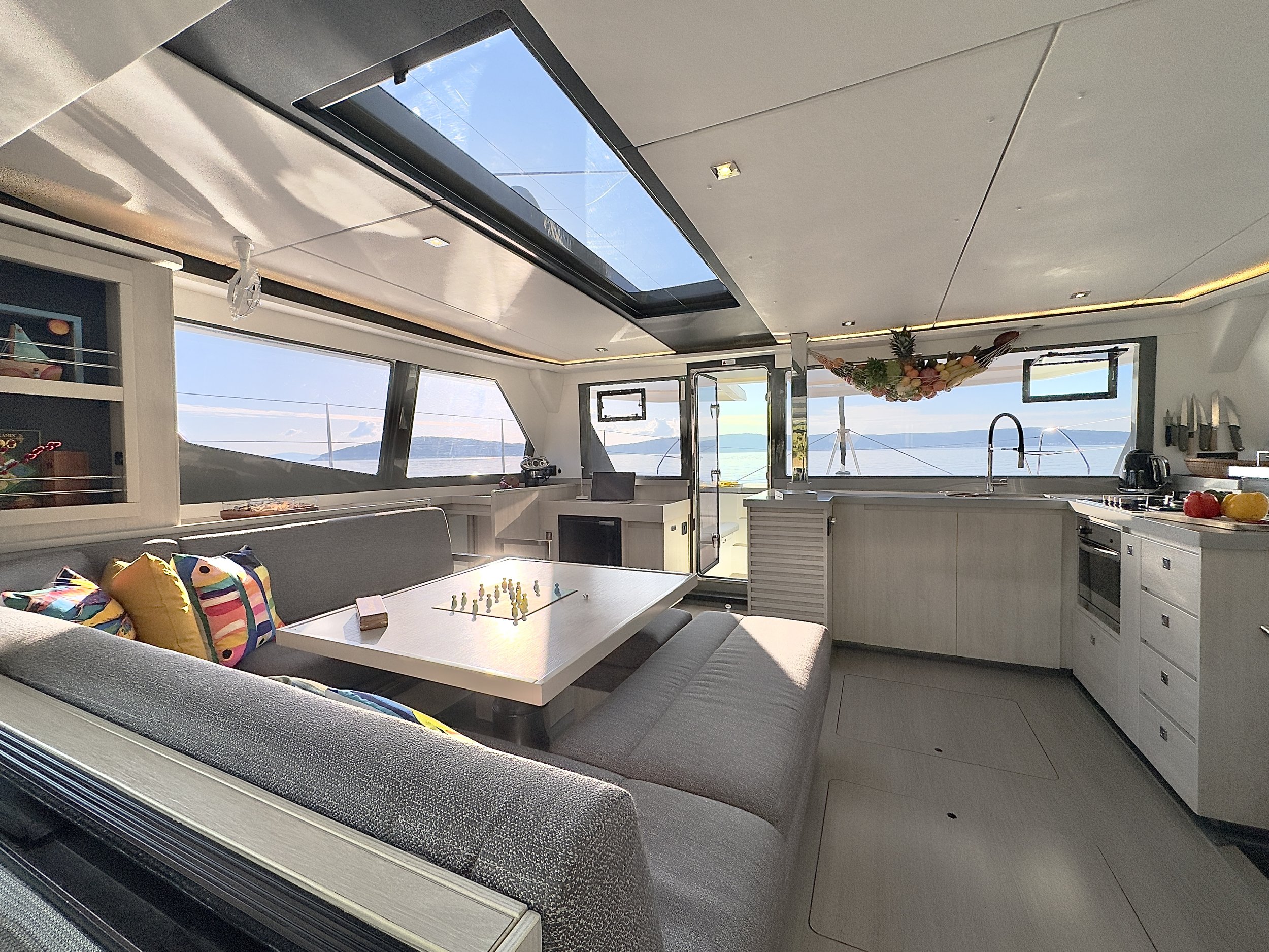 Interior of a modern yacht with a sitting area, a kitchen, and windows with a view of the sea and sky.