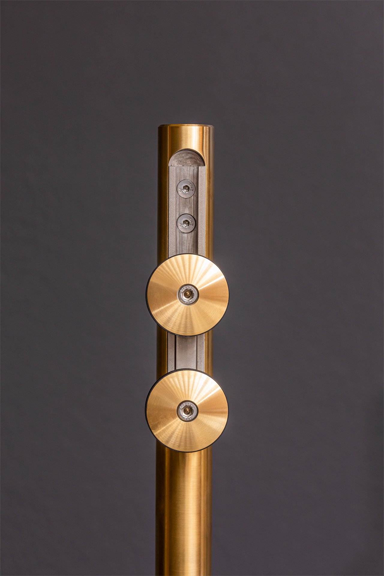 Close-up of a modern, metallic, gold-colored stand or pole with circular gold accents on a dark gray background.