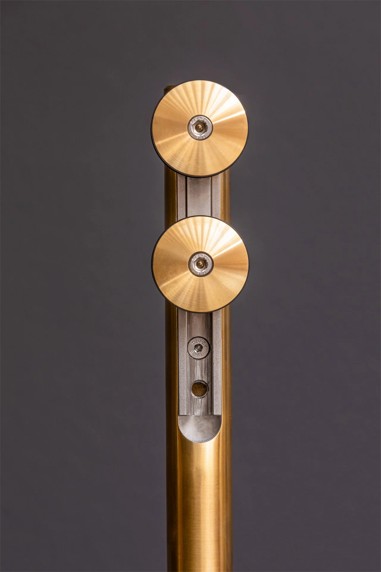 Close-up of a metallic mechanical device with two gold-colored circular components mounted vertically on a vertical pole against a dark gray background.