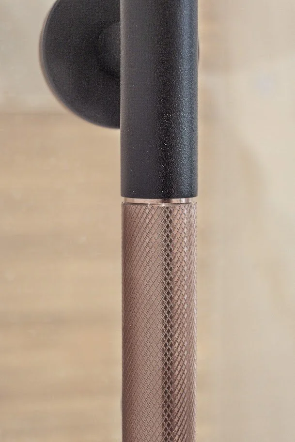 Close-up of a lighting fixture, showing a black cylindrical part attached to a textured, copper-colored lamp arm