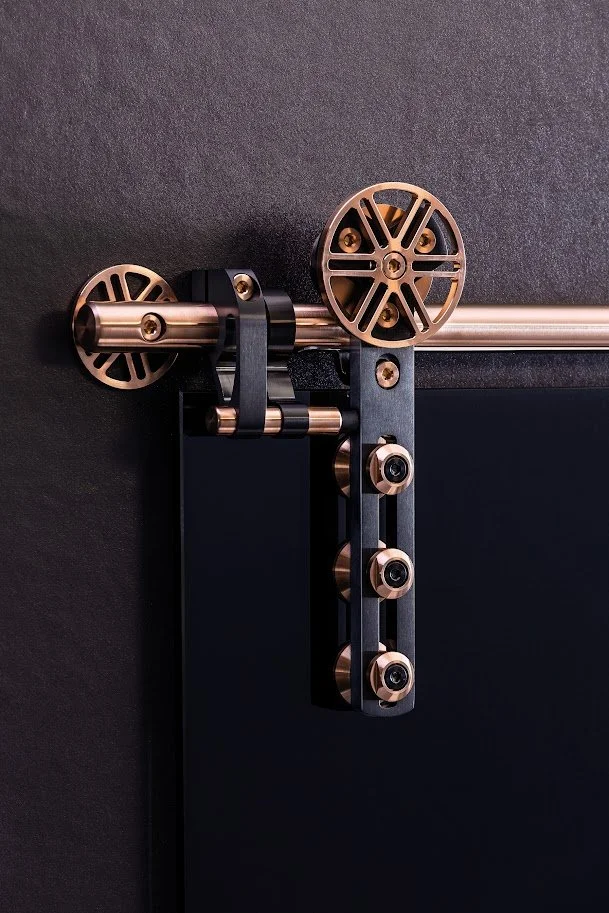 Close-up of a black sliding door with a modern roller hardware system in black and rose gold, mounted on a black wall.