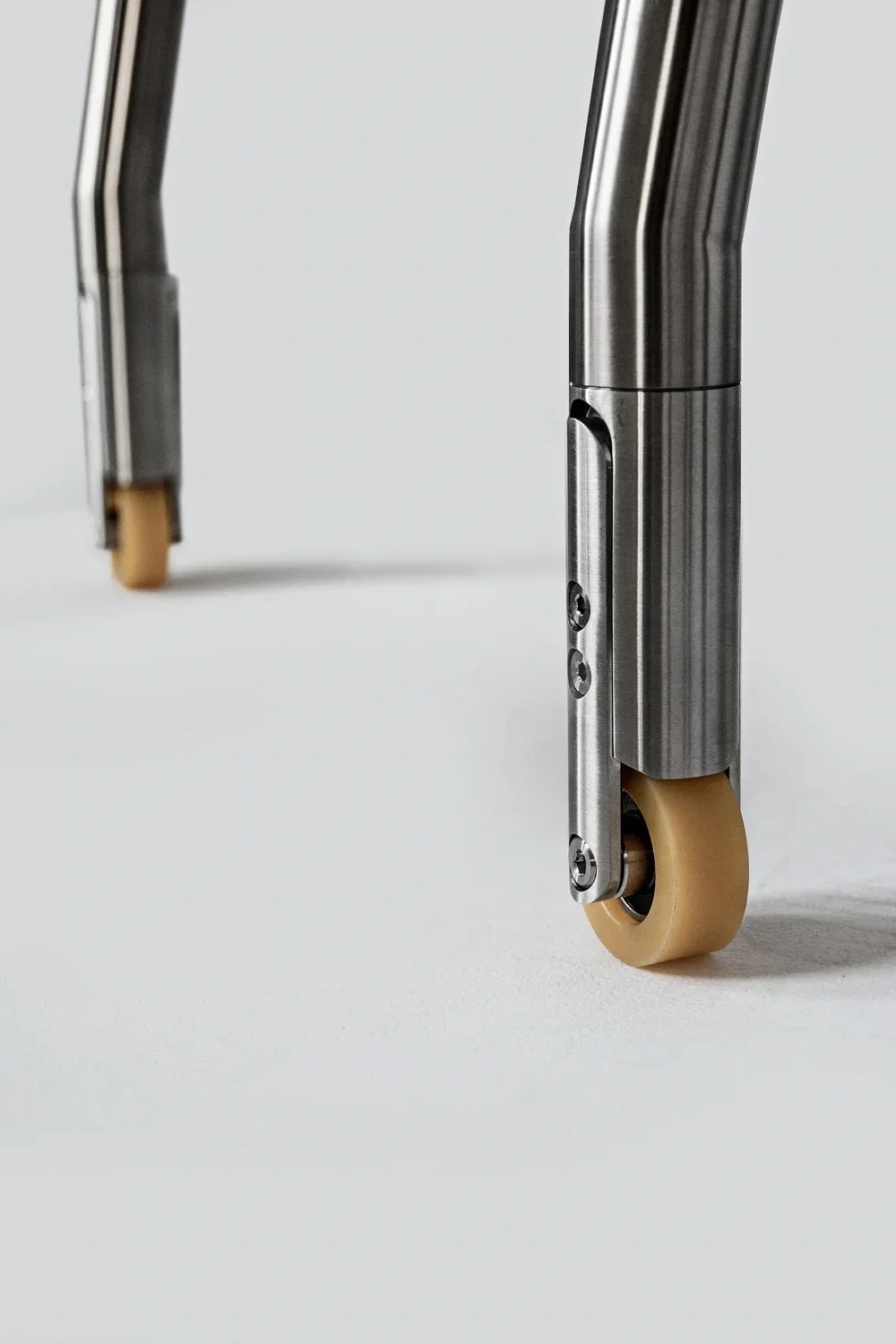 Close-up view of wheelchair caster wheels with metal support and beige tires on a white surface.