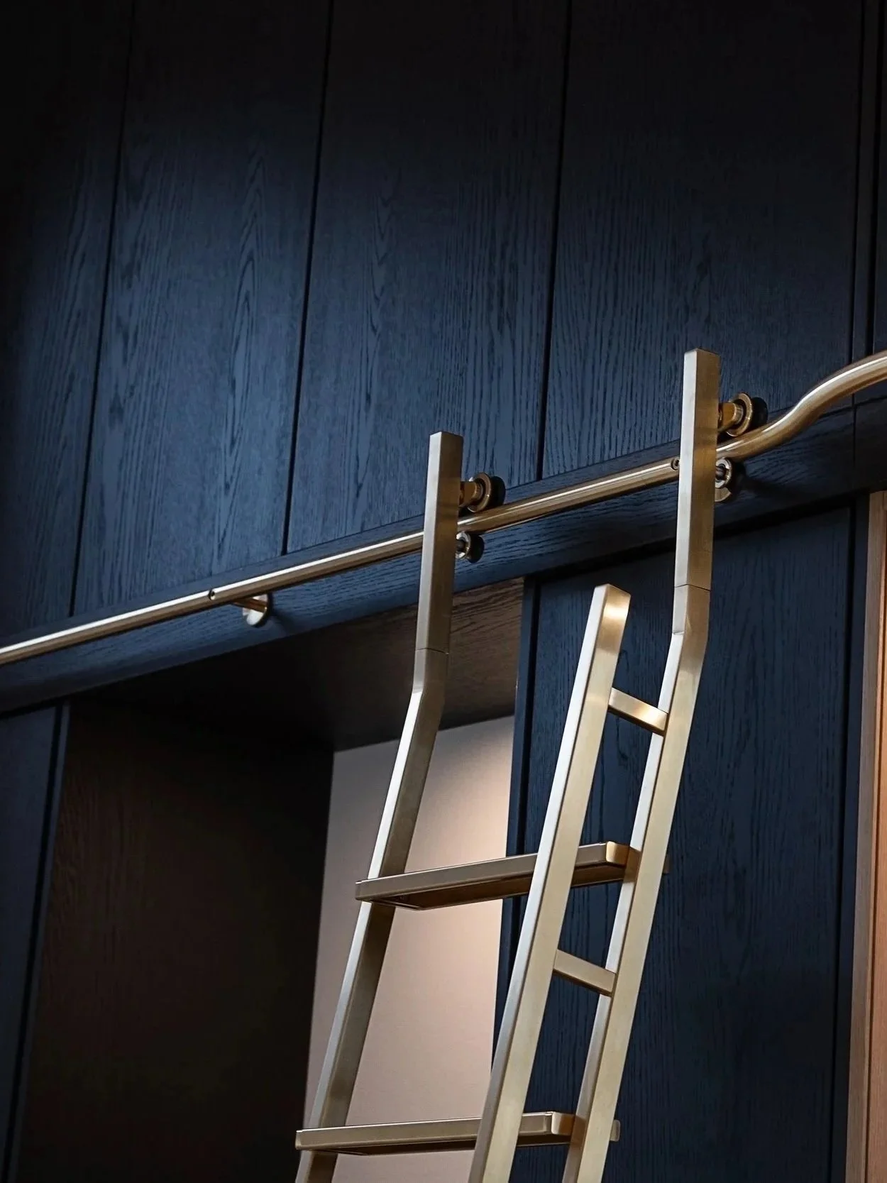 A ladder leaning against a dark wood cabinet with a metallic bar and rollers installed underneath.
