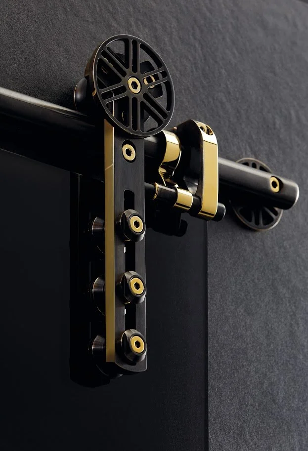Close-up of a sliding barn door hardware with black and gold rollers and track mounted on a dark wall.