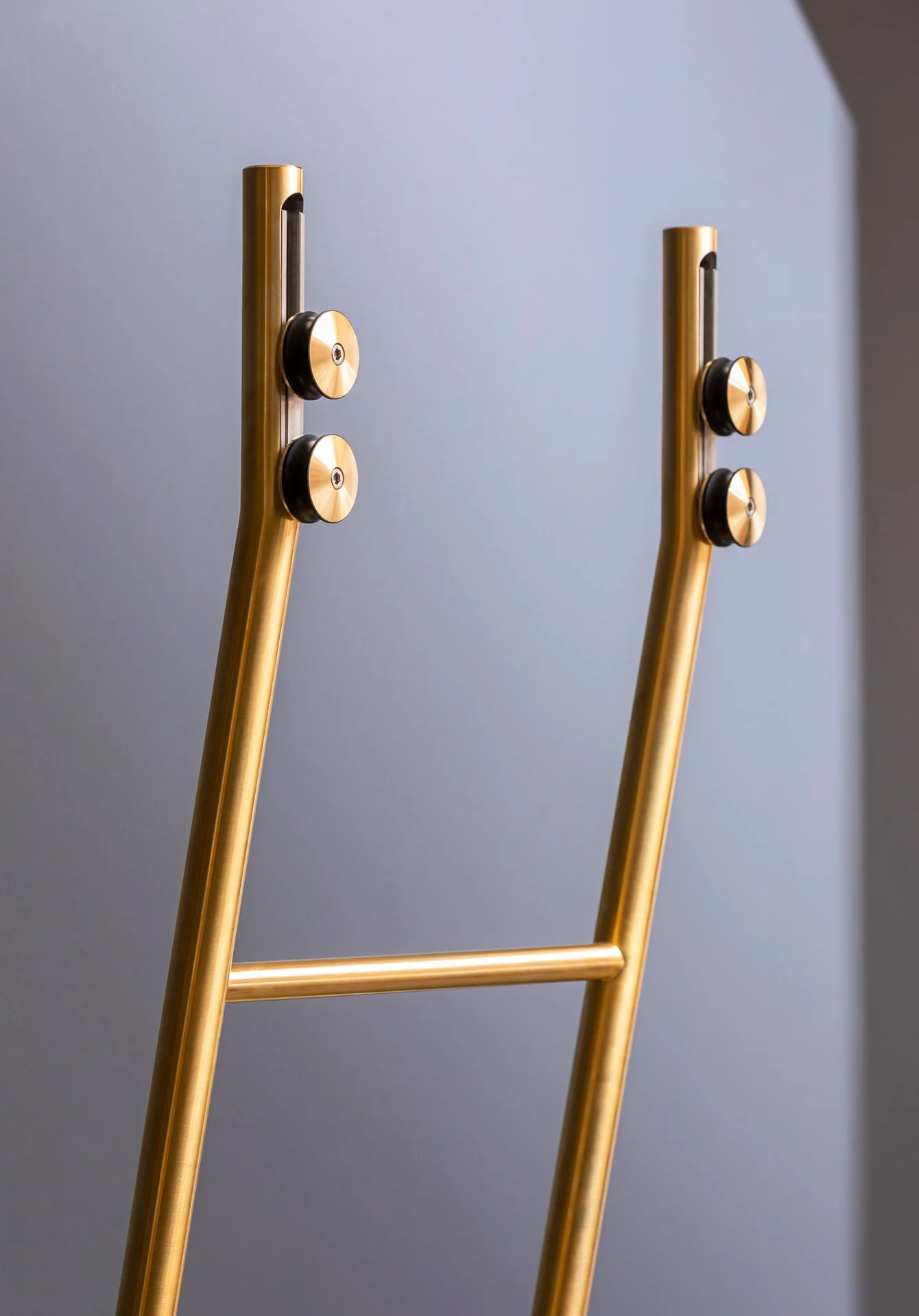 Two modern gold and black furniture legs or supports against a plain gray wall.