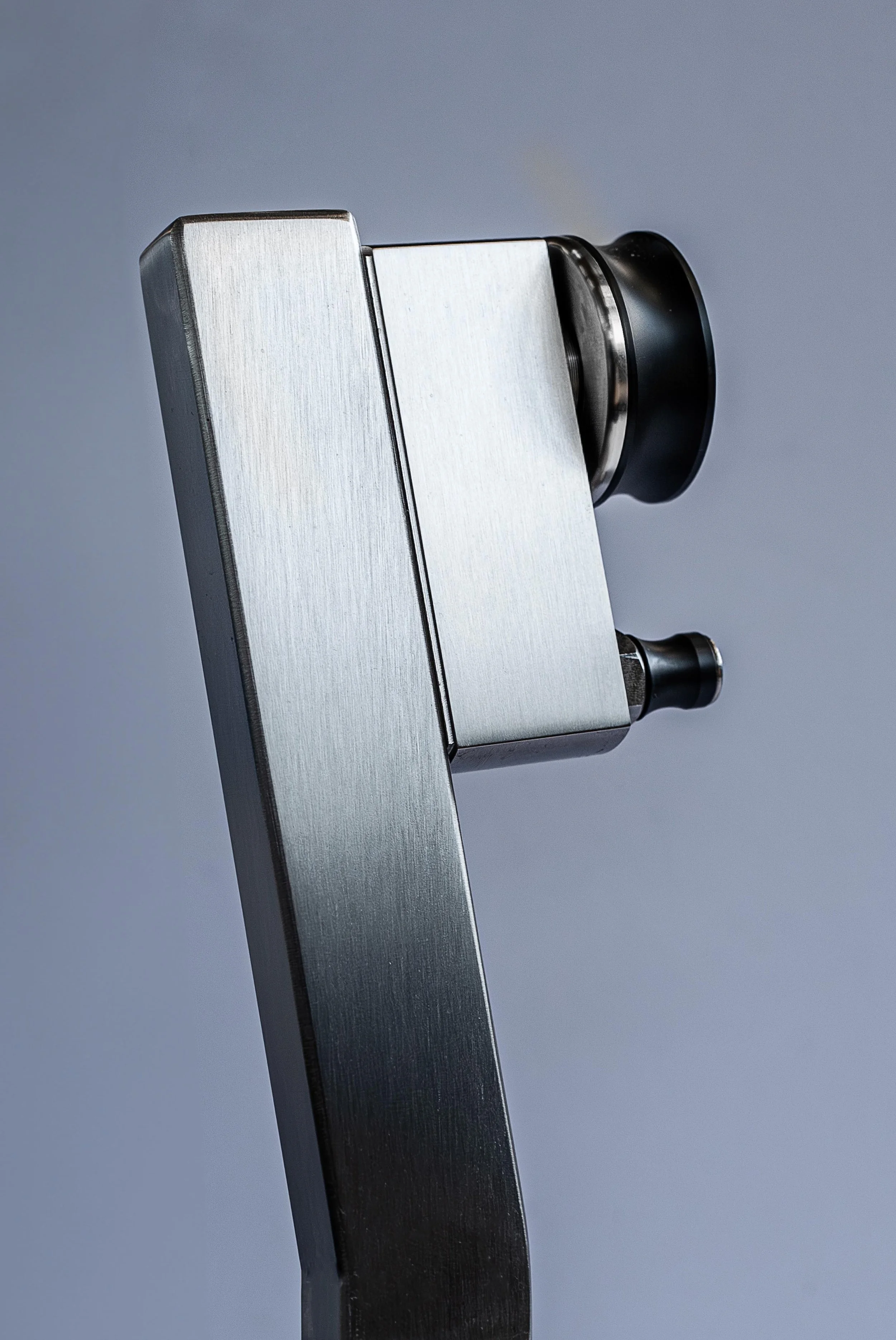Close-up of a silver metallic microscope focusing on the black adjustment knob and objective lens against a plain gradient background.