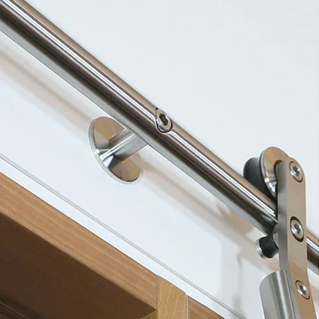 Close-up of a stainless steel handrail mounted on a white wall, attached with a metal bracket near a wooden surface.